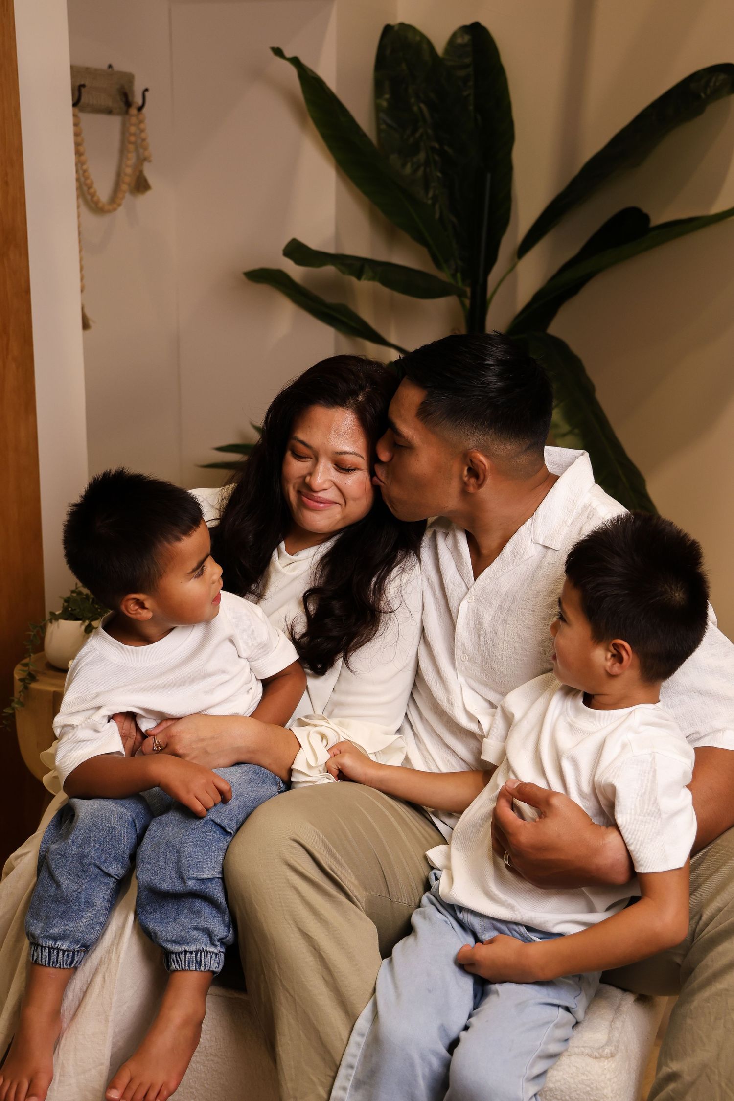 A family wearing white shirts and jeans cuddles together on a couch in a warm, intimate home setting.