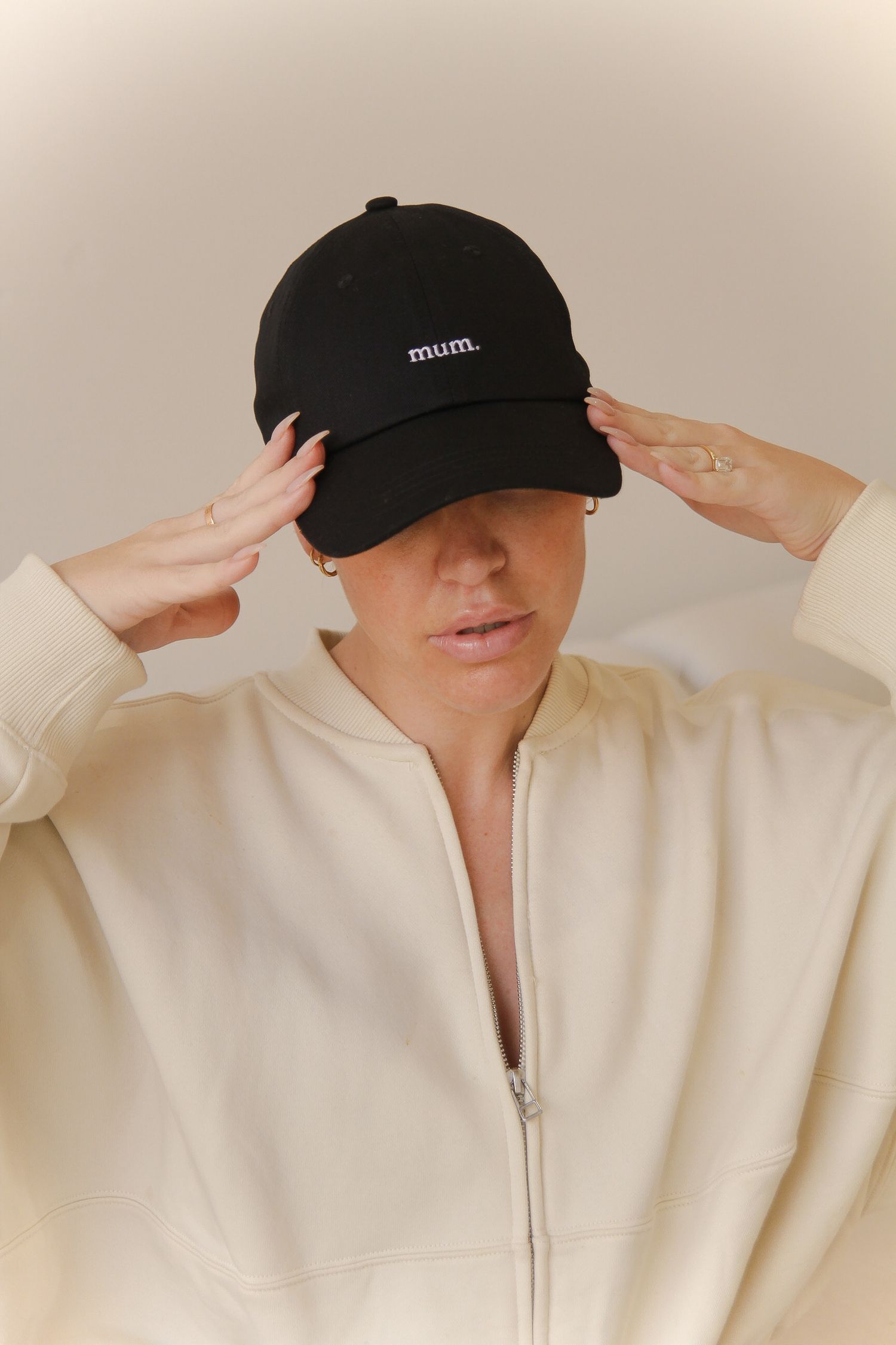 Person wearing cream hoodie and black baseball cap with minimal branding.