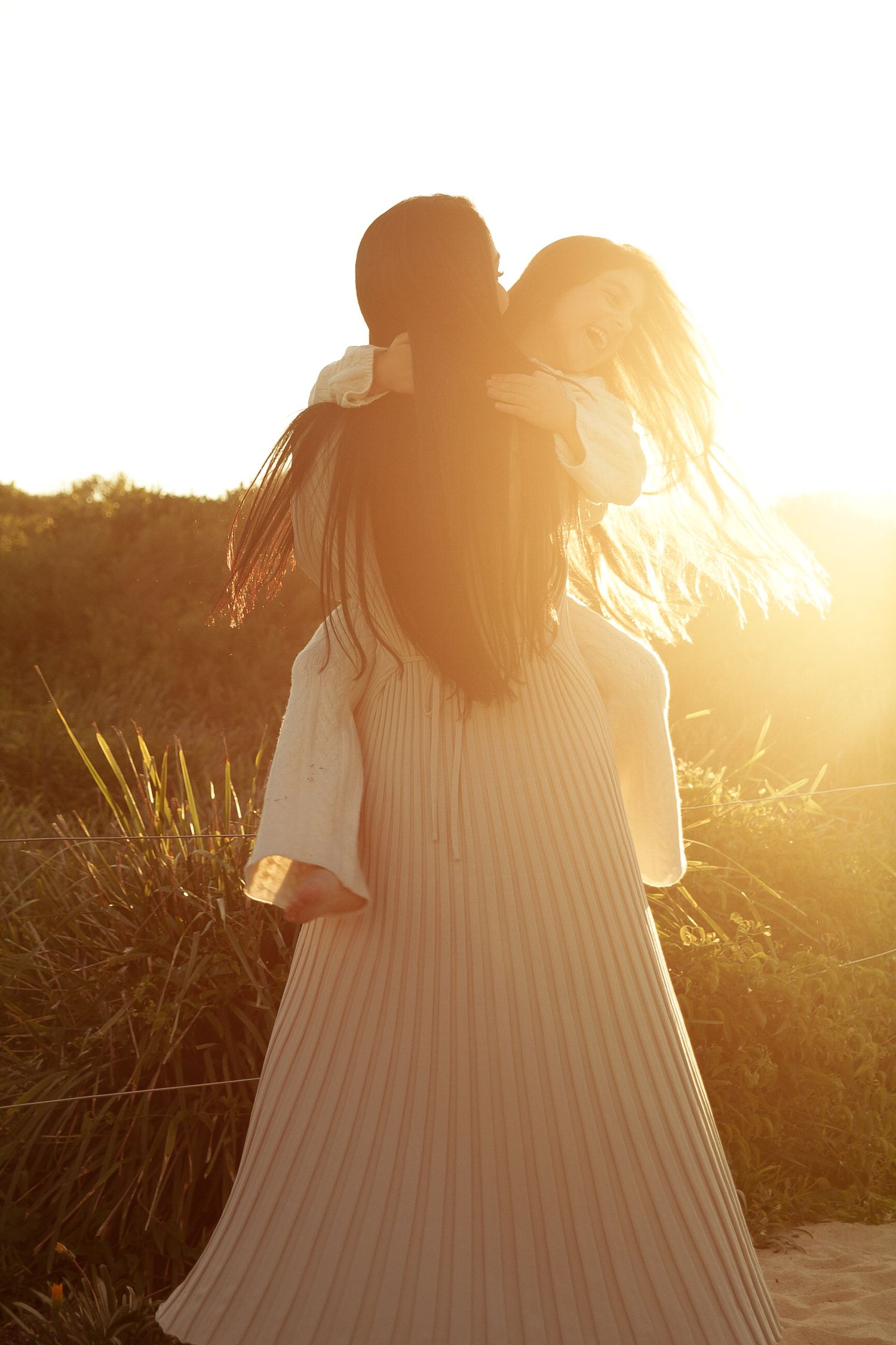Silhouette of figures in flowing dresses against a golden sunset on the beach.
