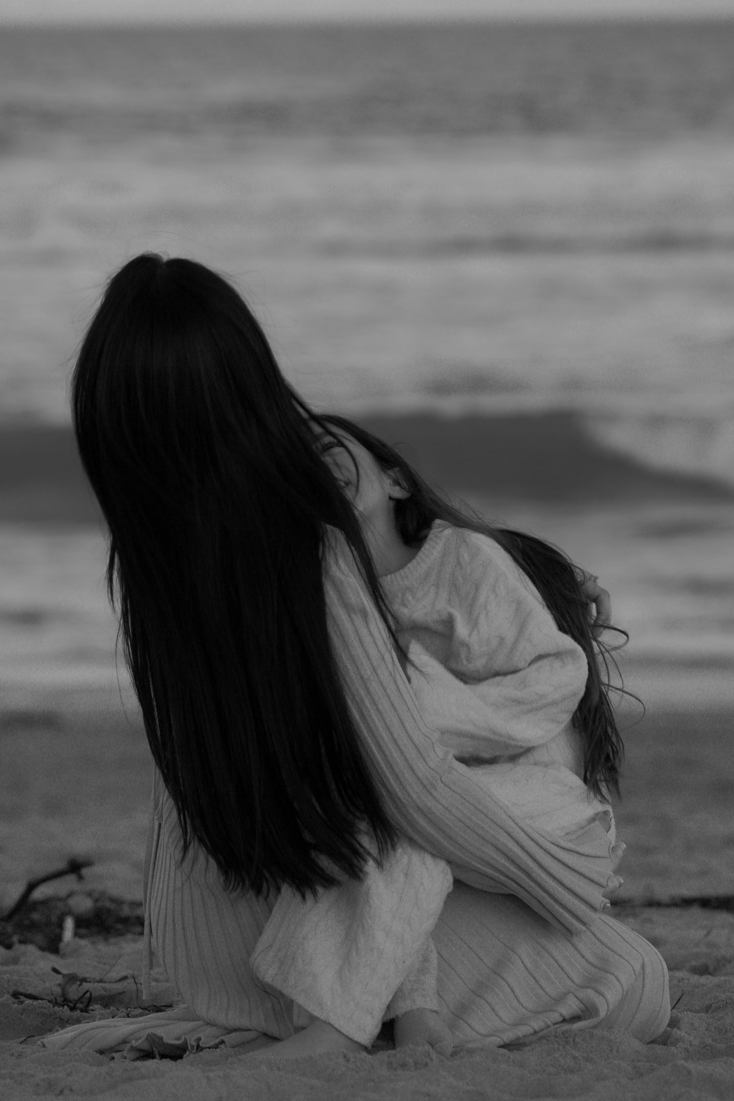 Woman in white dress laying artistically on beach sand in black and white photography.