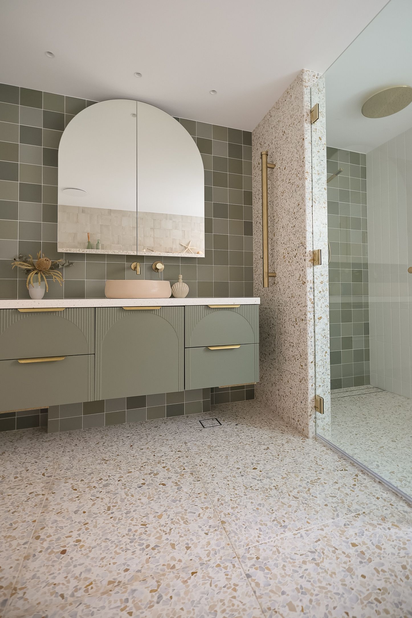 Modern bathroom with sage green tiles, floating vanity, and terrazzo flooring.