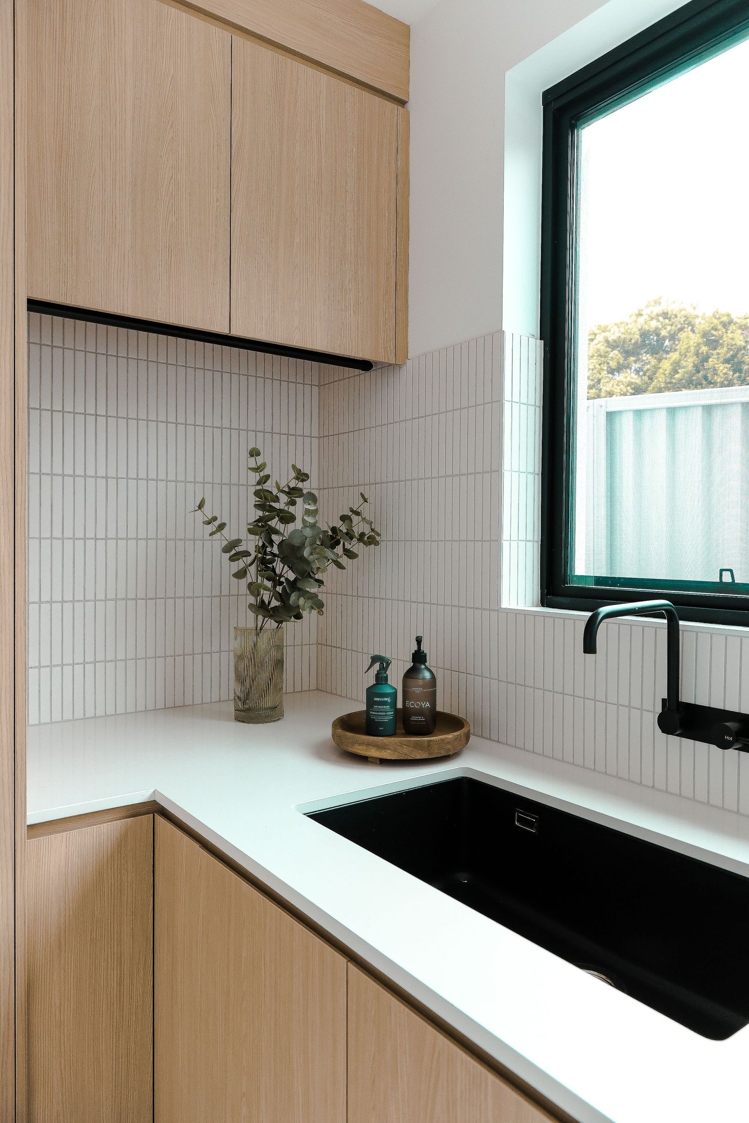 Modern minimalist kitchen with light wood cabinets, white tile backsplash, and black fixtures.