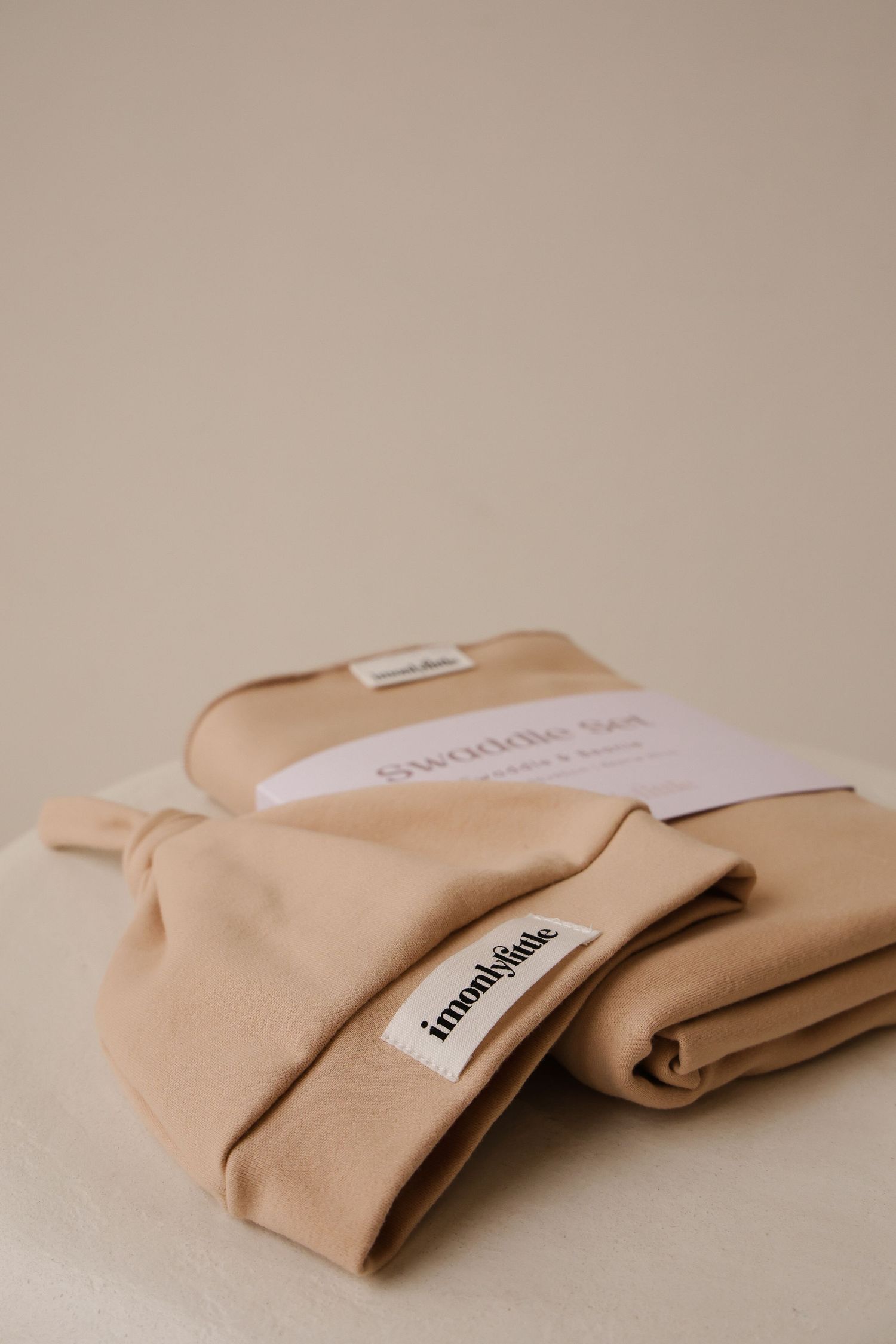 Folded beige baby clothing items with brand label against neutral background.