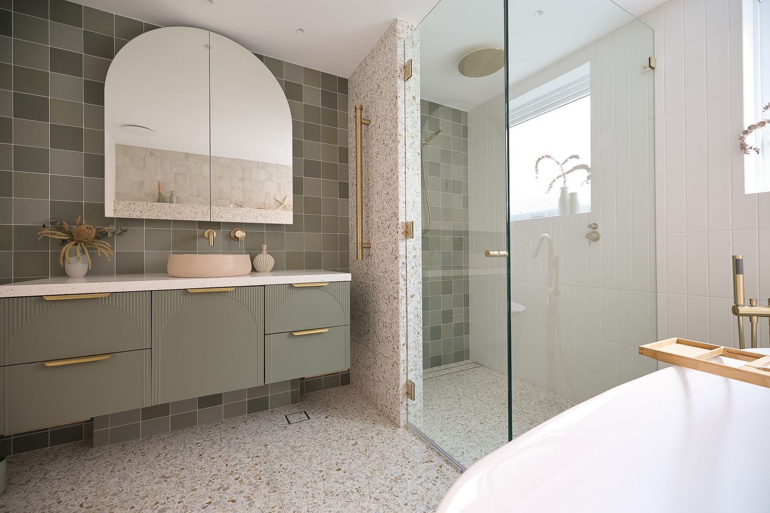 Spacious bathroom featuring sage green tiles, arched mirror, and glass shower enclosure.