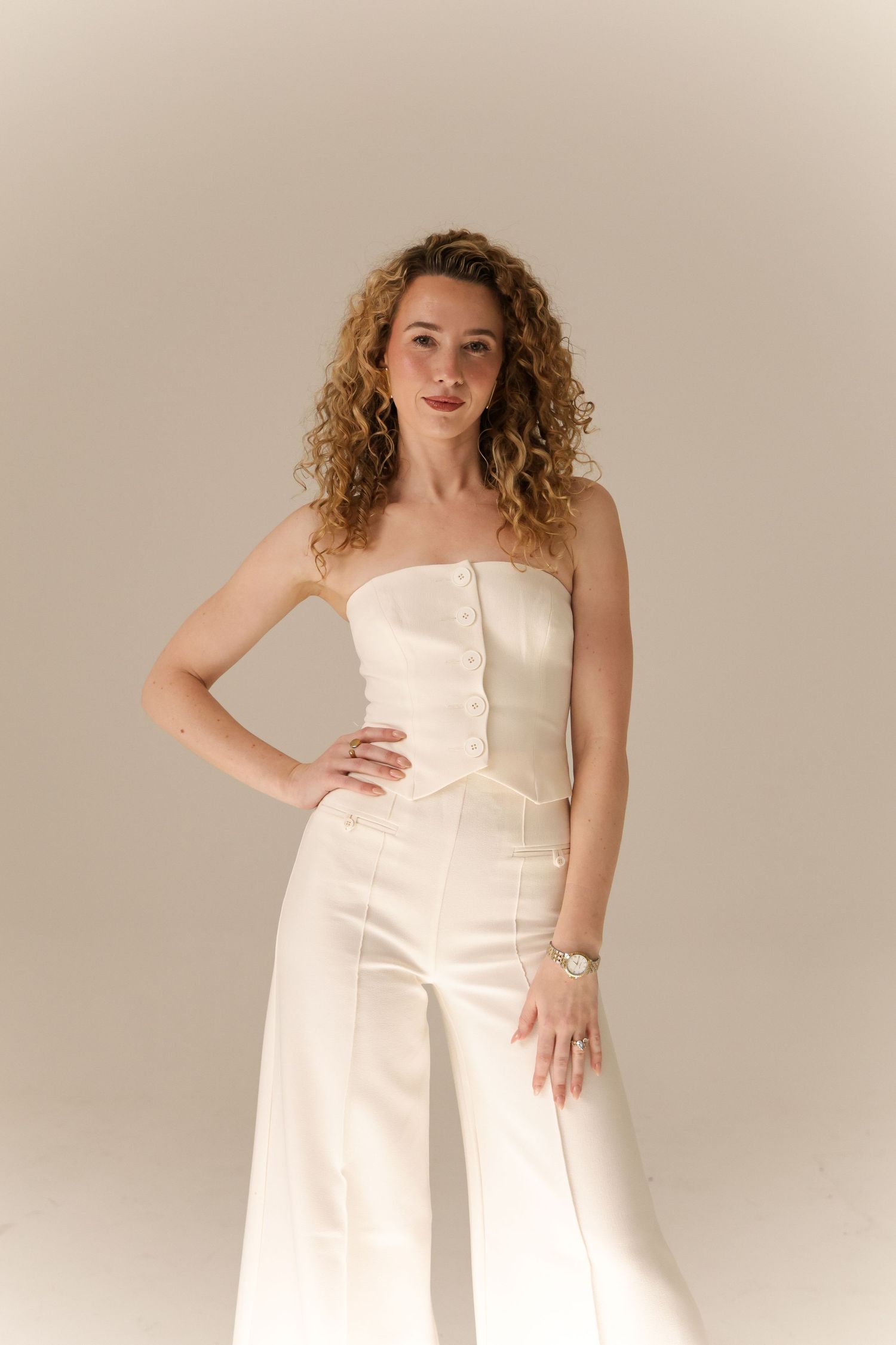 Studio portrait featuring someone in white strapless jumpsuit striking confident pose.