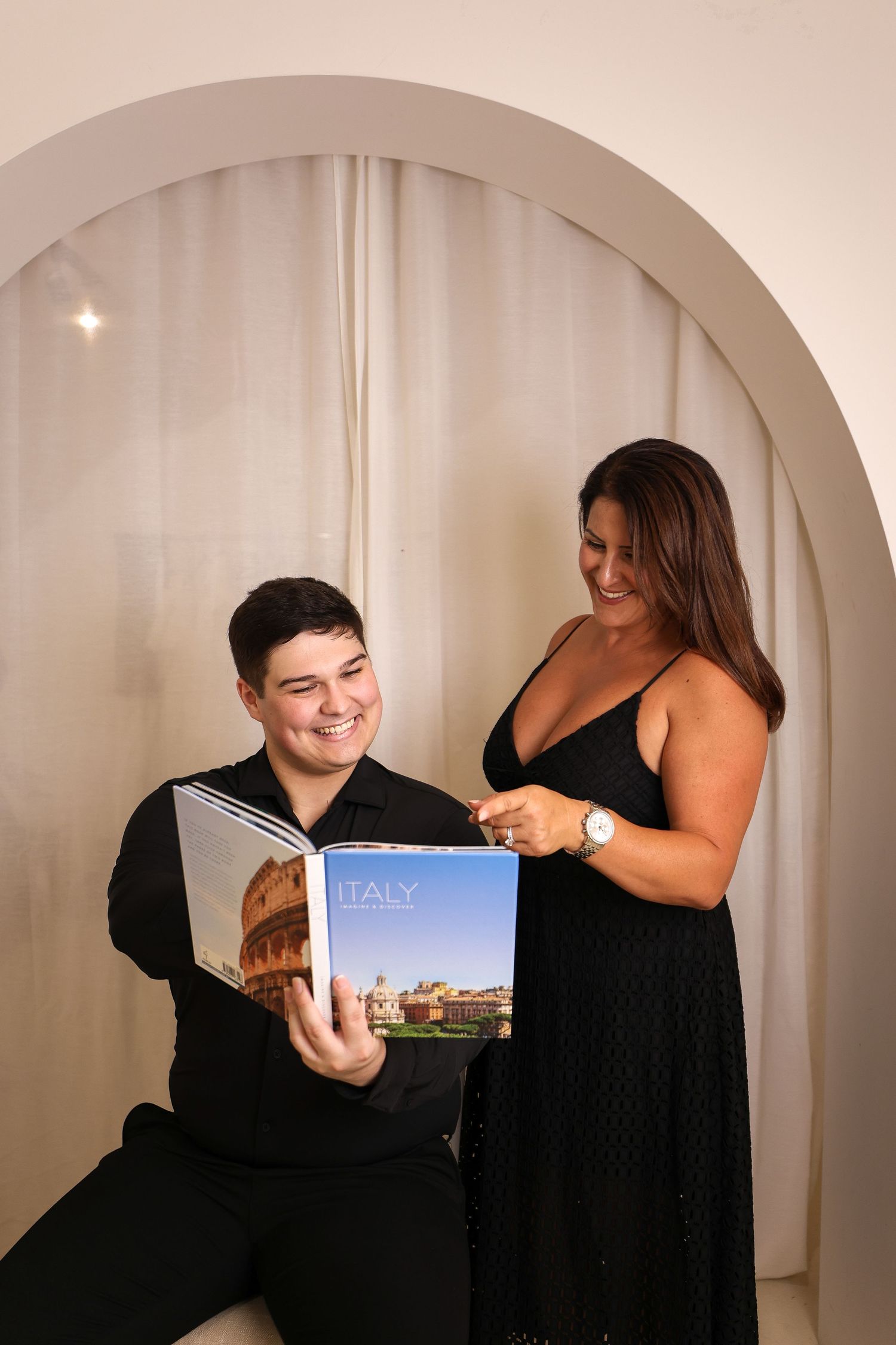 Two people excitedly looking at Italy travel book under arched doorway.