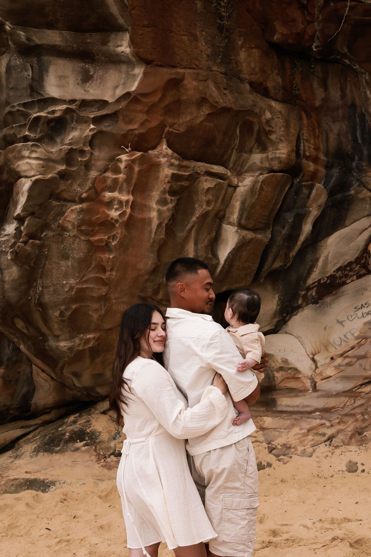 A family embraces against dramatic rock formations wearing coordinating white outfits.