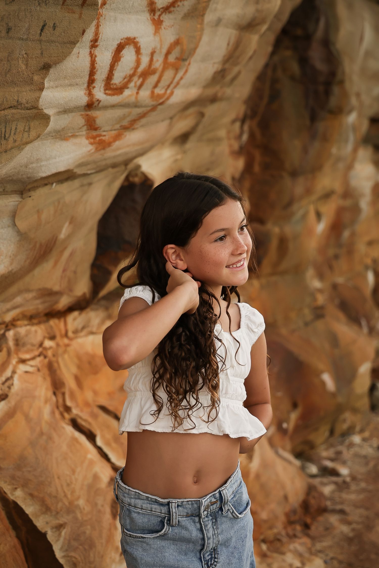 Young woman posing against sandstone rock wall in crop top and jeans.