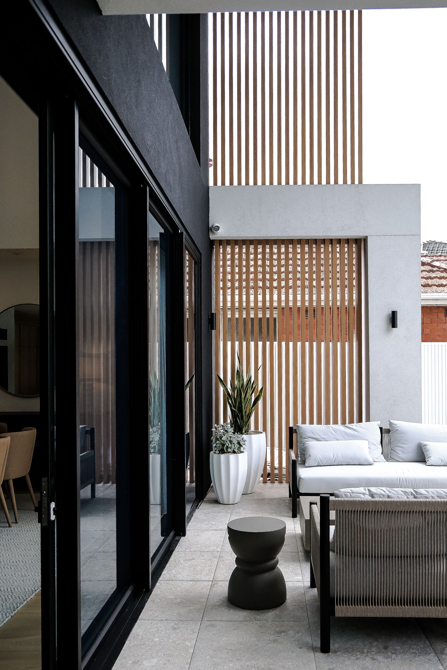 Modern patio with slatted wood screens, black frames, and comfortable outdoor seating.