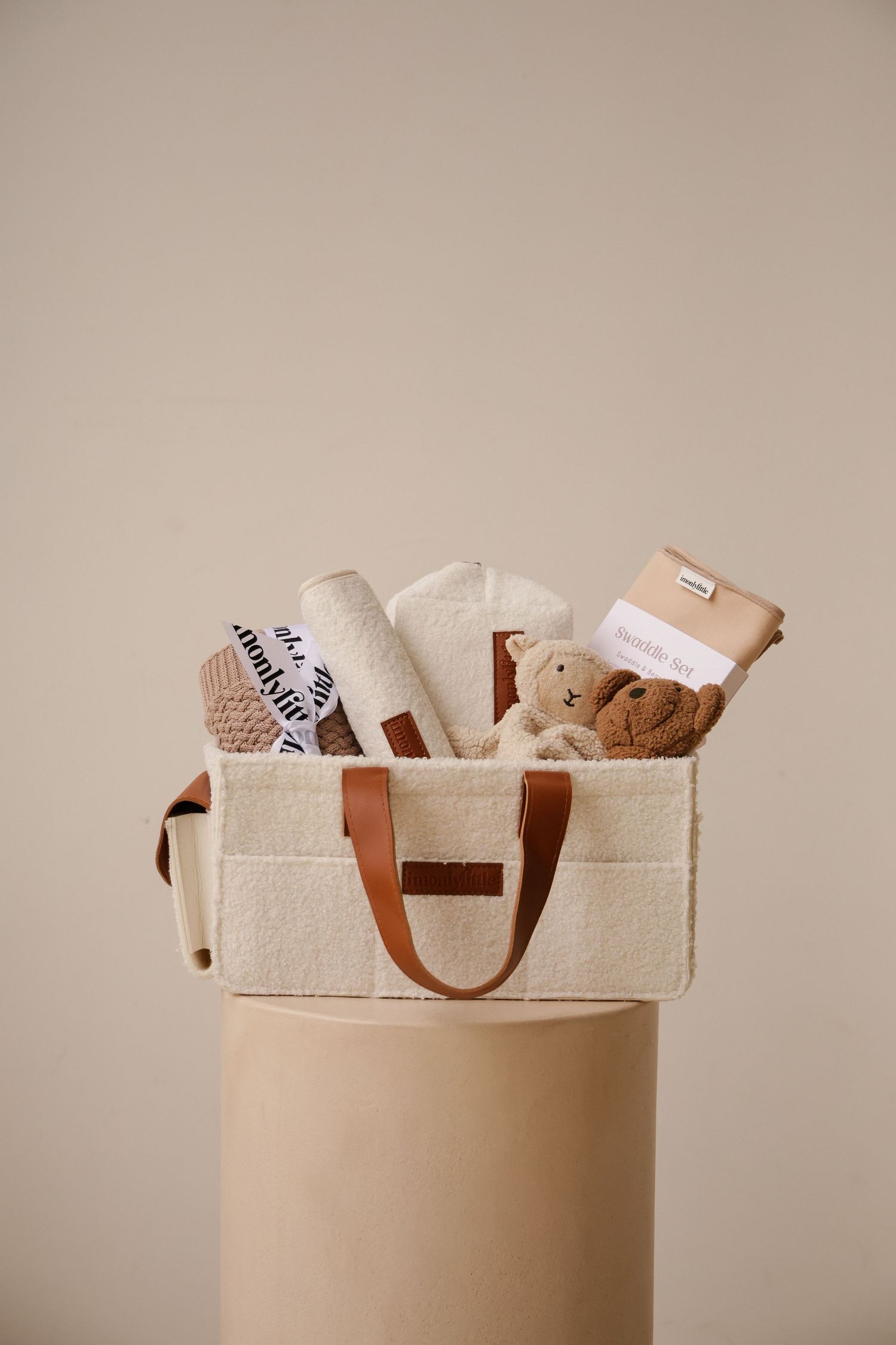 Cream storage bag filled with baby essentials and plush toys on beige pedestal.