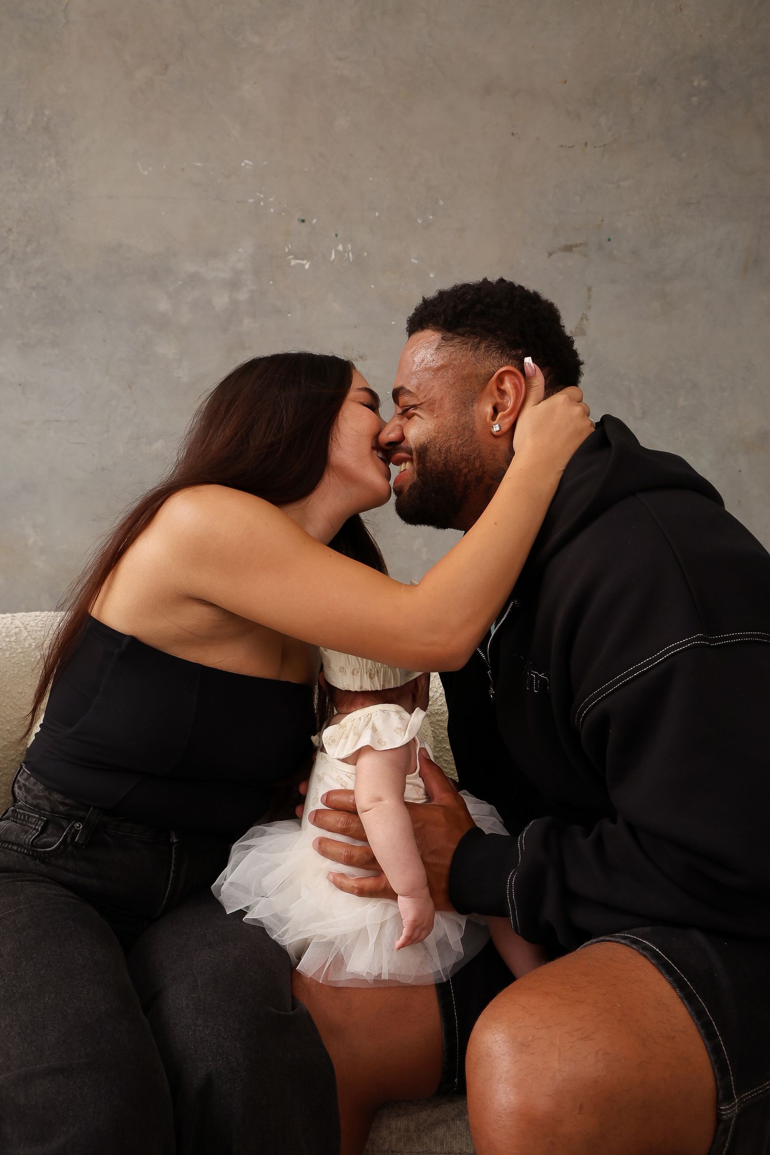 A loving couple shares an affectionate moment while holding their baby in a tulle dress.
