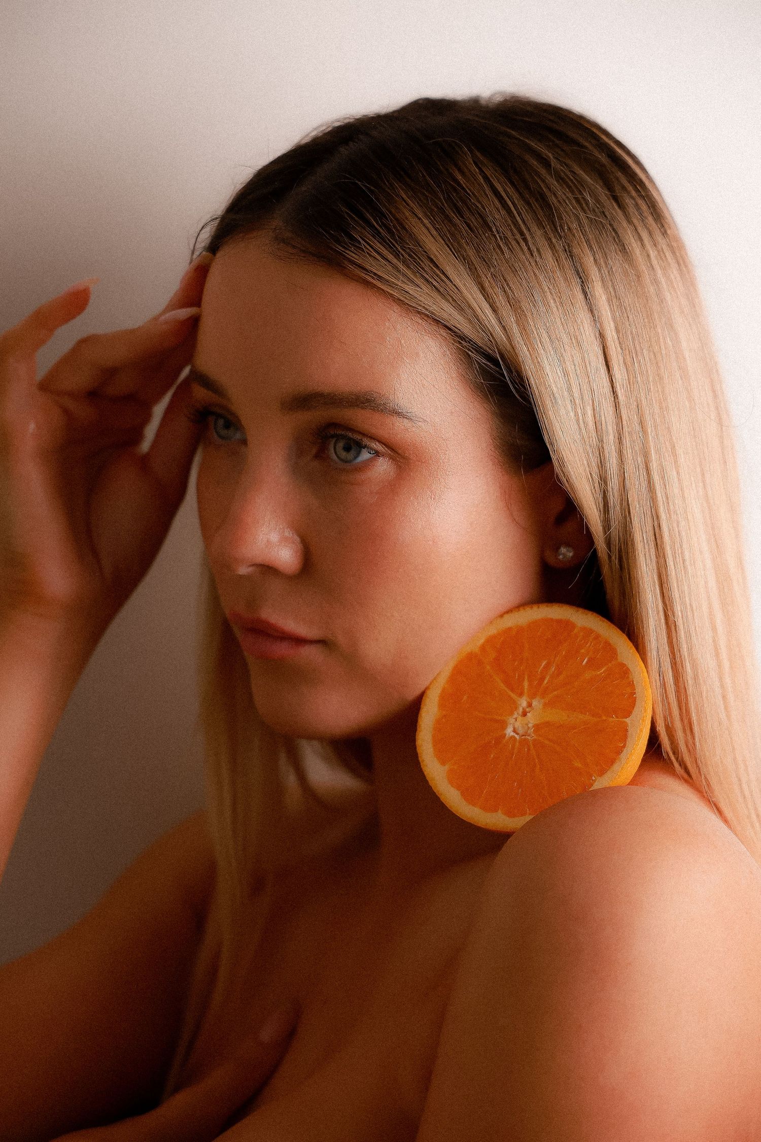 A creative portrait series showing a person posing with an orange slice held against their ear like an earring.