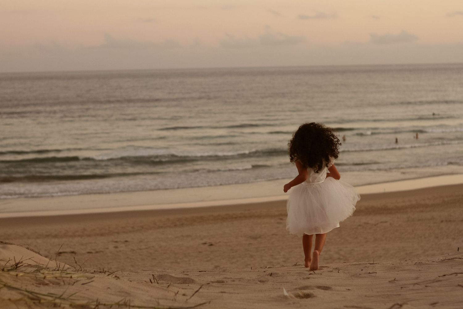Person in white dress walks alone on beach at dusk.