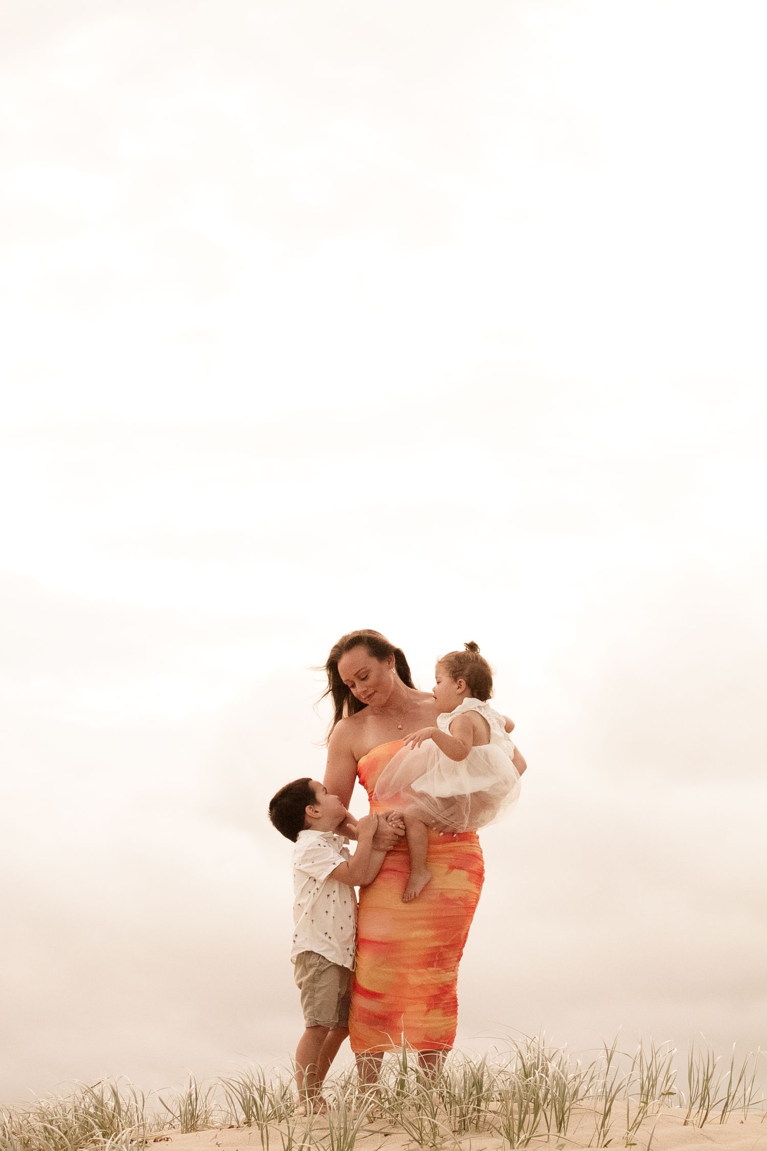 Family members share joyful moments together against a sunset beach backdrop with sand dunes.