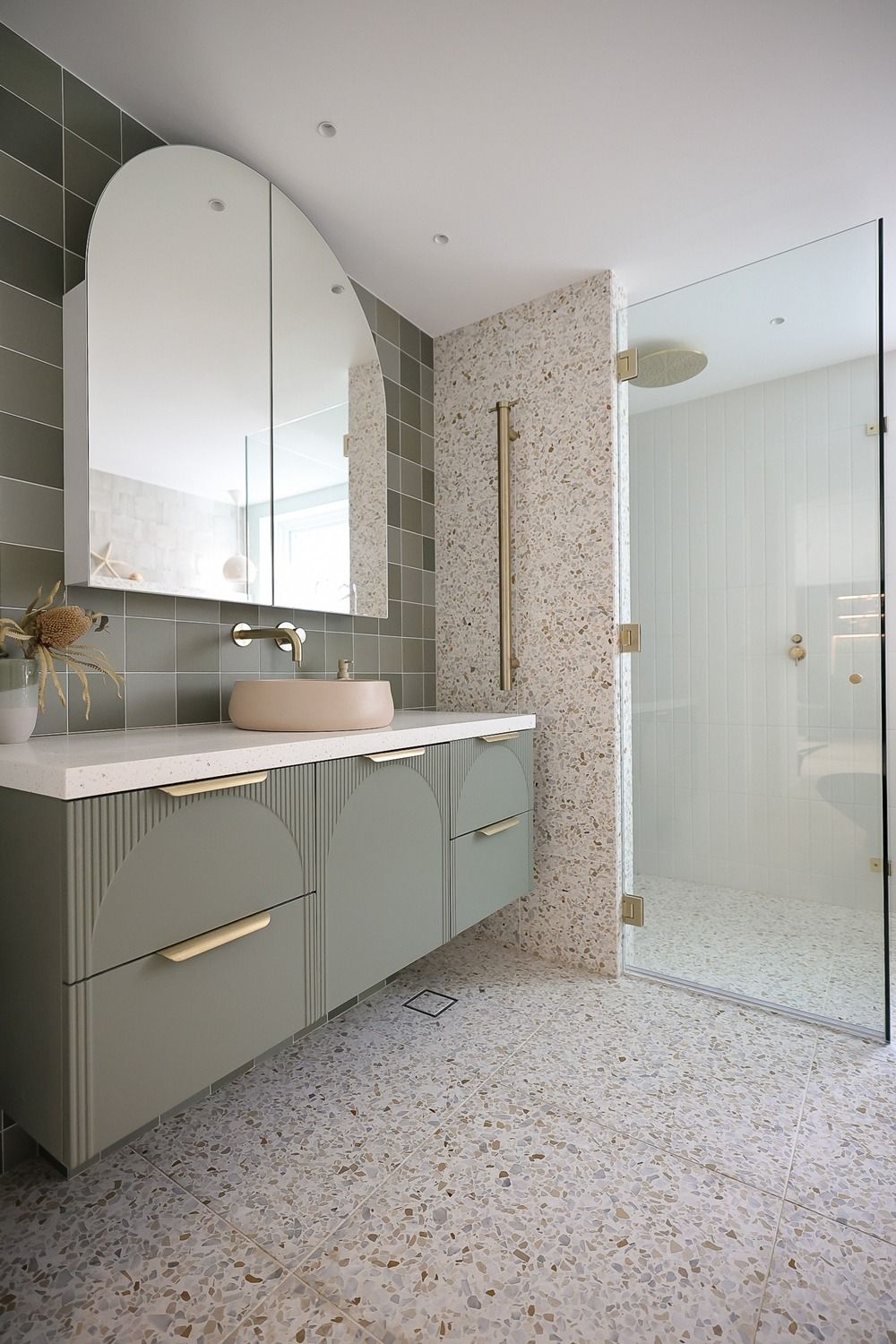 Modern bathroom interior with sage green cabinets, terrazzo flooring, and minimalist white walls and fixtures.