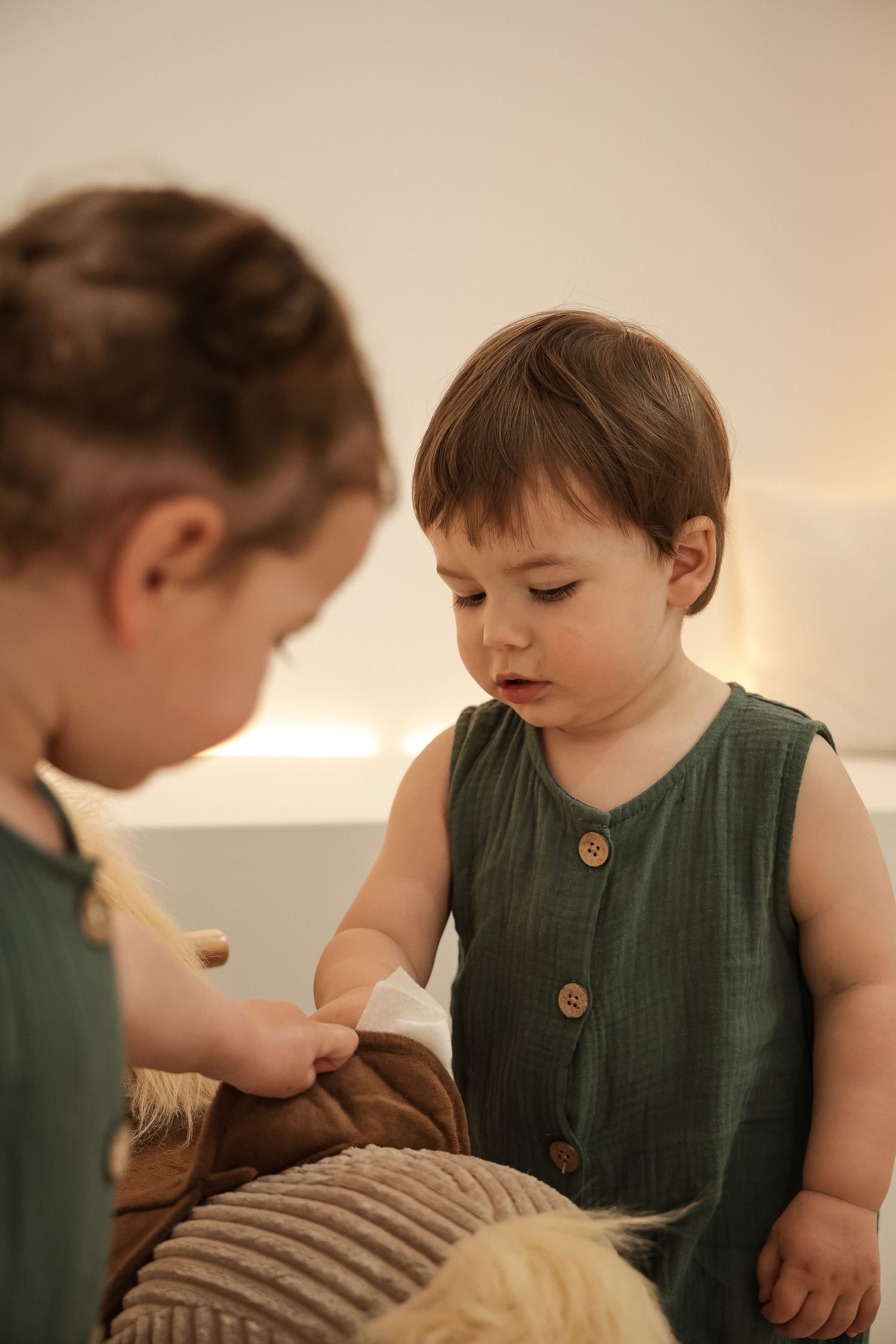 Two small children in matching green outfits playing with toys on a beige surface.