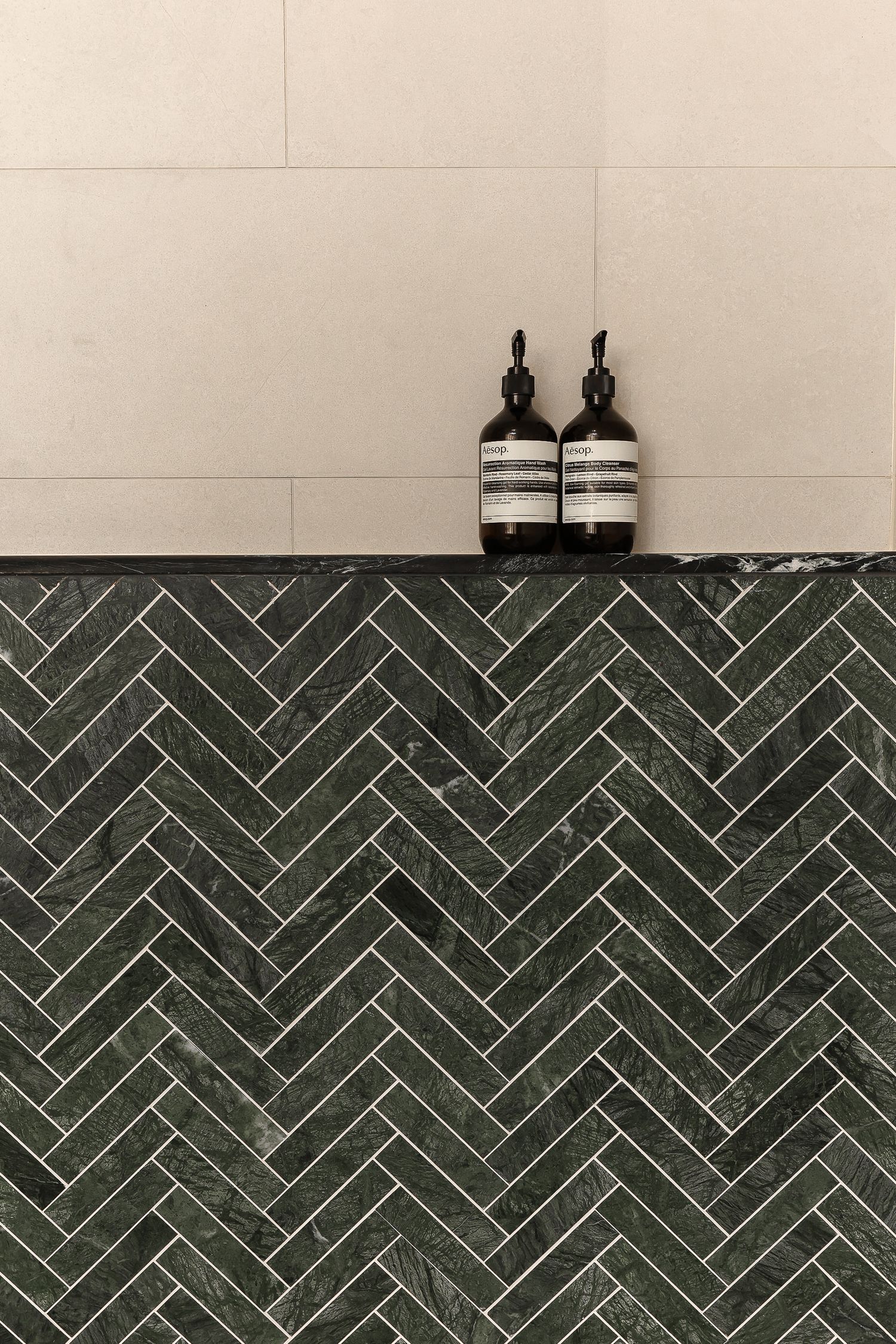 Dark green herringbone tile pattern creates a striking backsplash with modern fixtures mounted above.