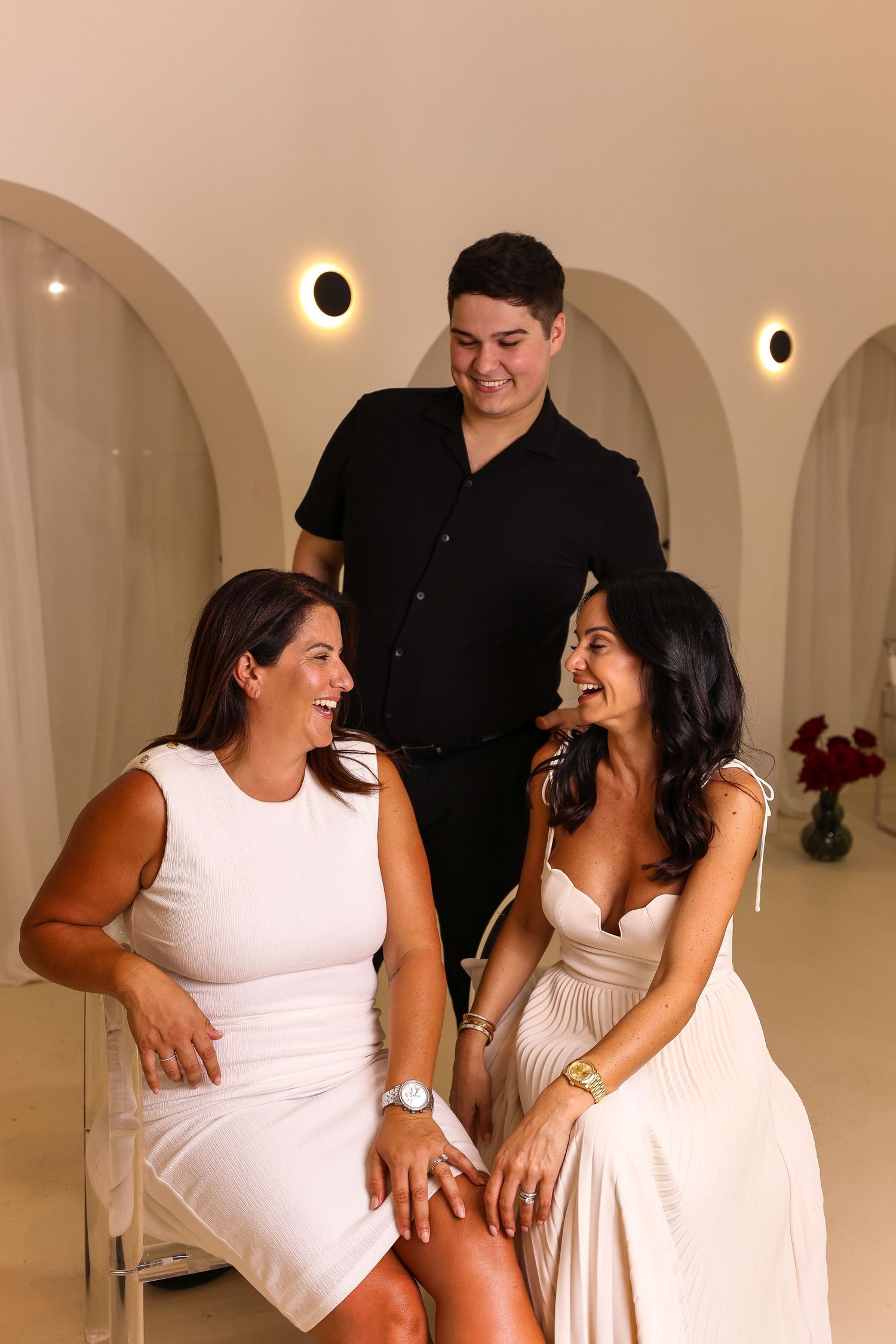 Three people sharing a candid moment in white minimalist room with arched details.