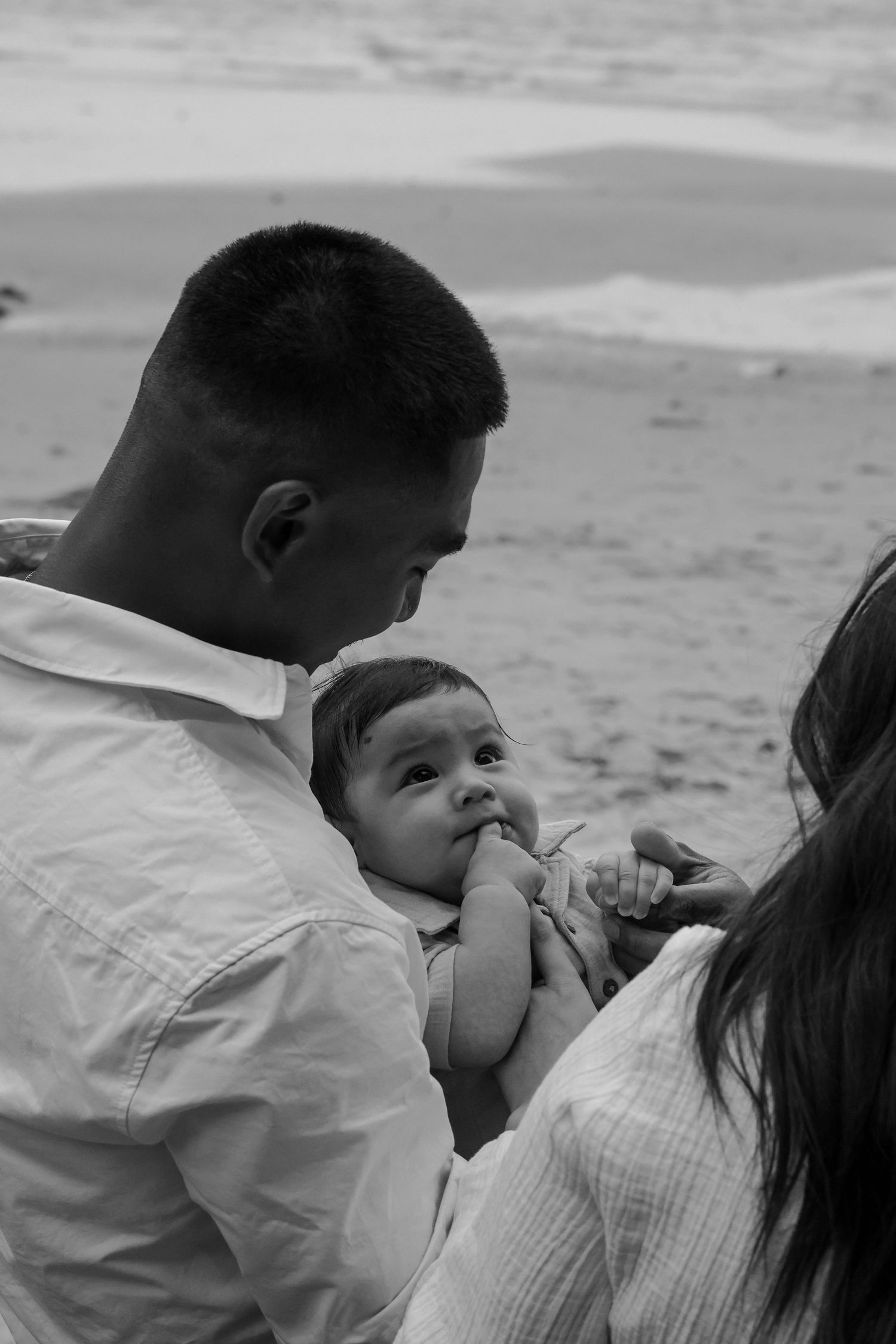 A black and white beach portrait of a family sharing an intimate moment.