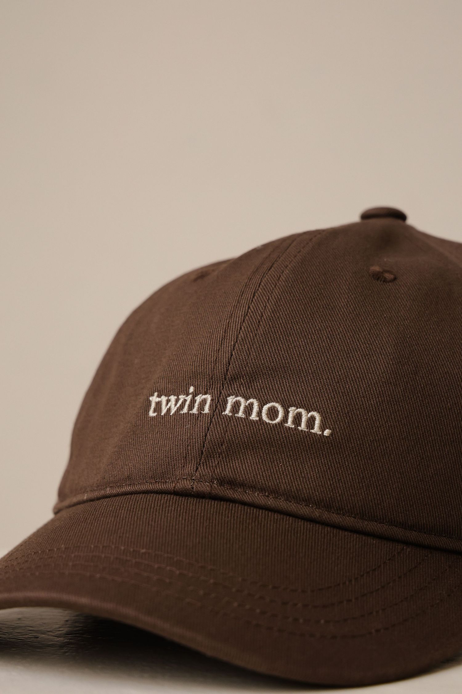 A brown baseball cap with 'twin mom' embroidered text on the front against a neutral background.