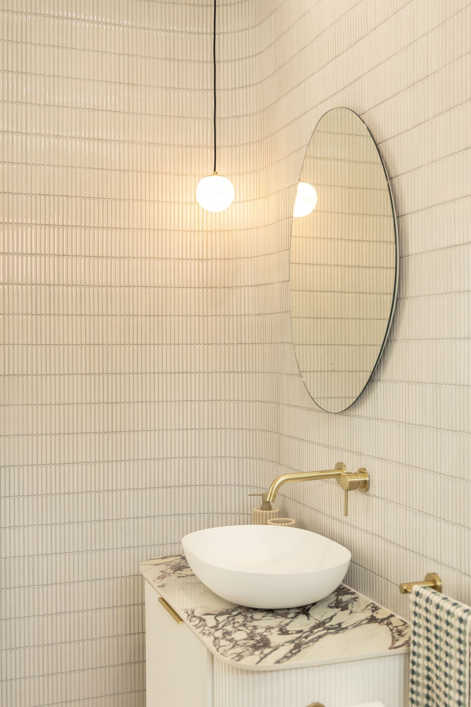 Modern bathroom featuring white textured tile walls, round mirror, and gold fixtures.