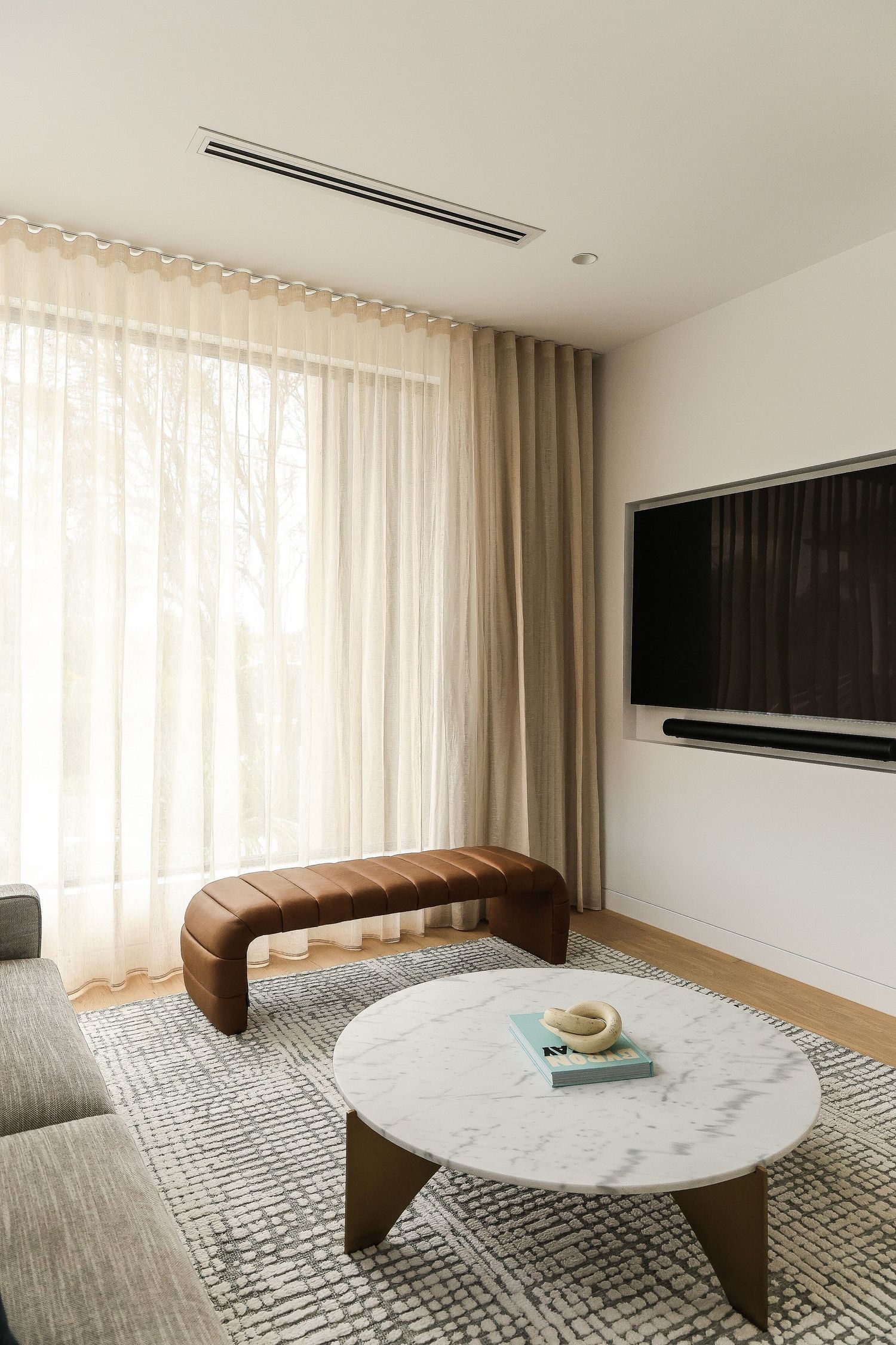 Modern living room with marble coffee table, curved bench, and sheer curtains.