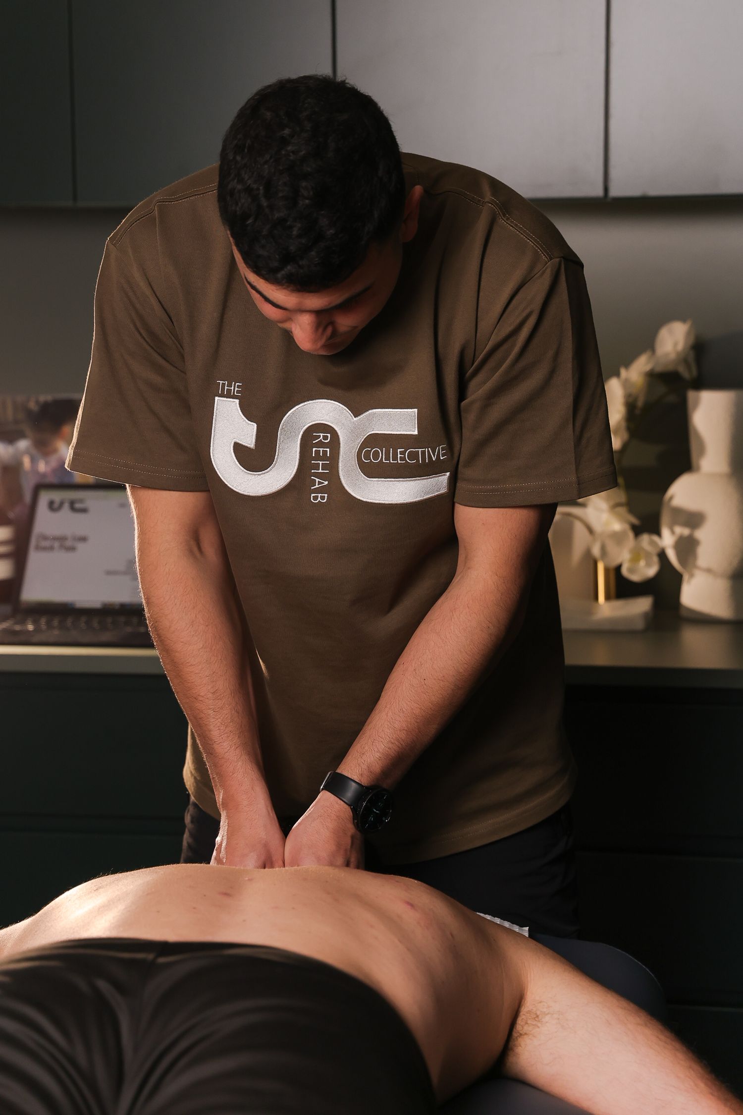 A massage therapist wearing a brown t-shirt performs therapeutic massage techniques on a client's back.