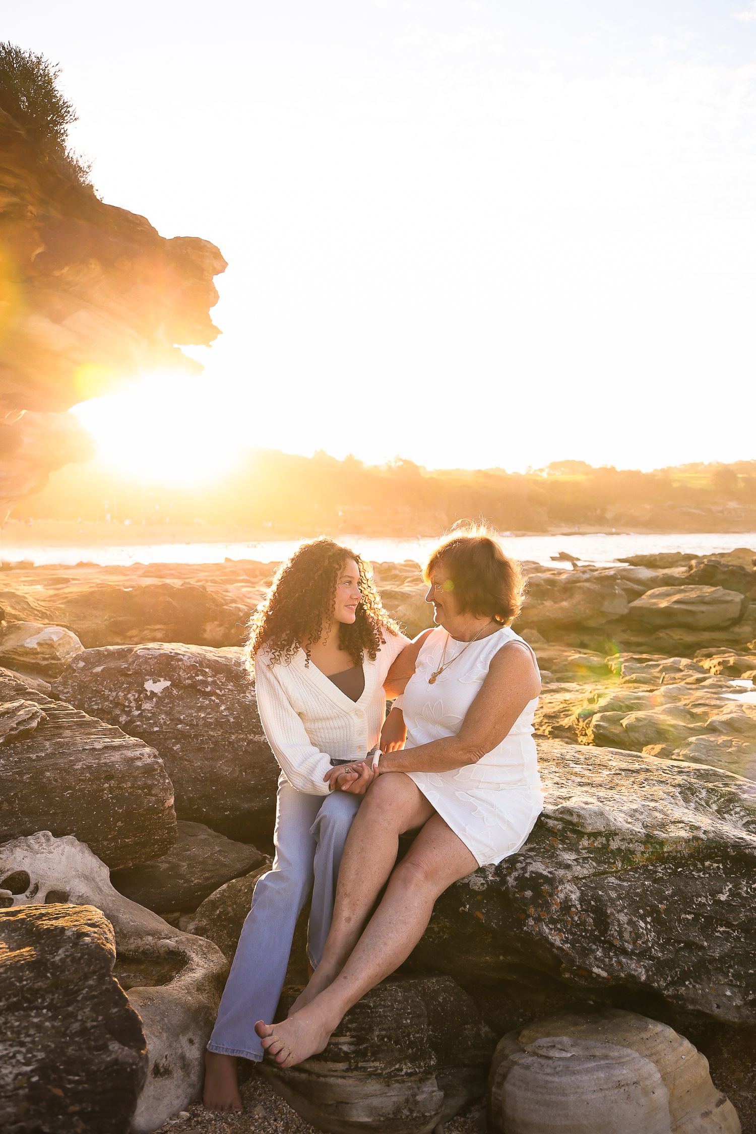 Couple sharing romantic moment on rocky beach during golden sunset.