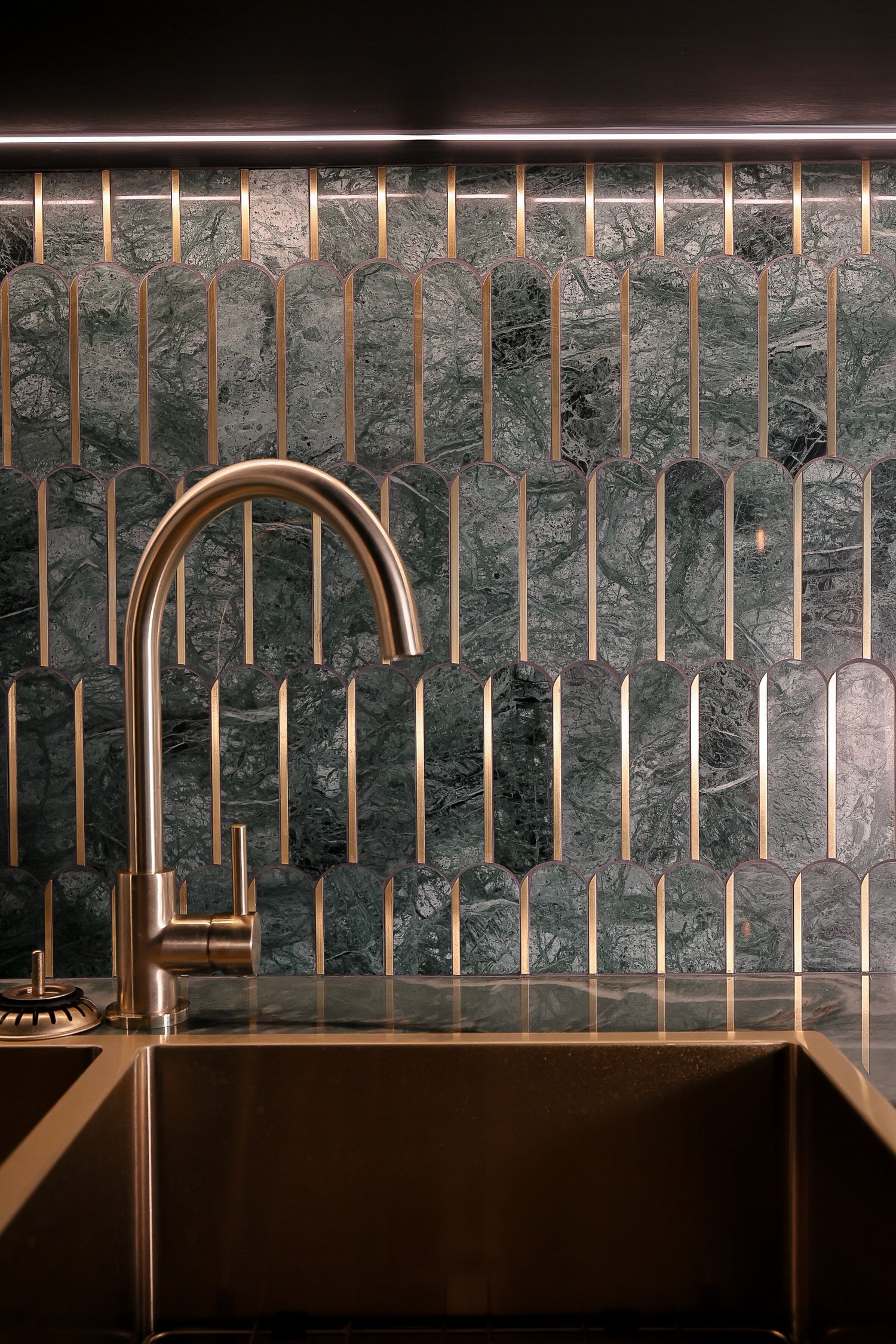Modern kitchen backsplash with vertical dark marble tiles and gold faucet.