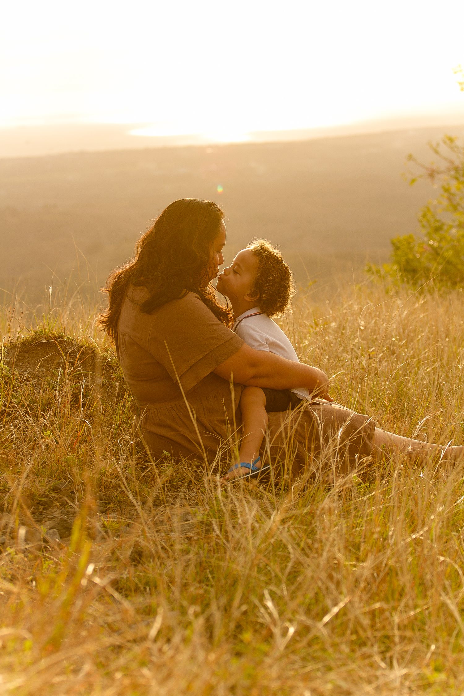 Mother and child share intimate moment in sunlit meadow at golden hour.