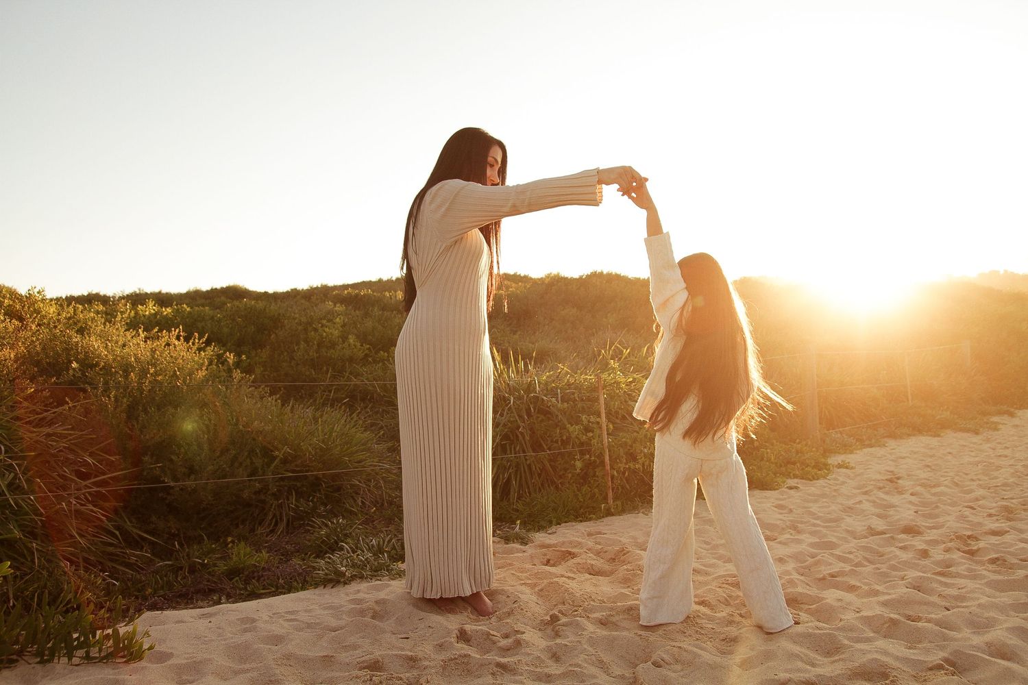 Two people dancing together on a sandy beach at sunset with golden light filtering through.