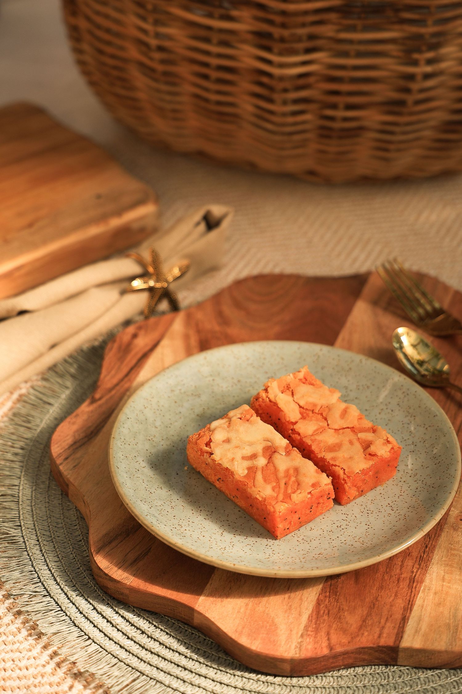 Two pink dessert bars on grey plate with wooden serving board and wicker basket.