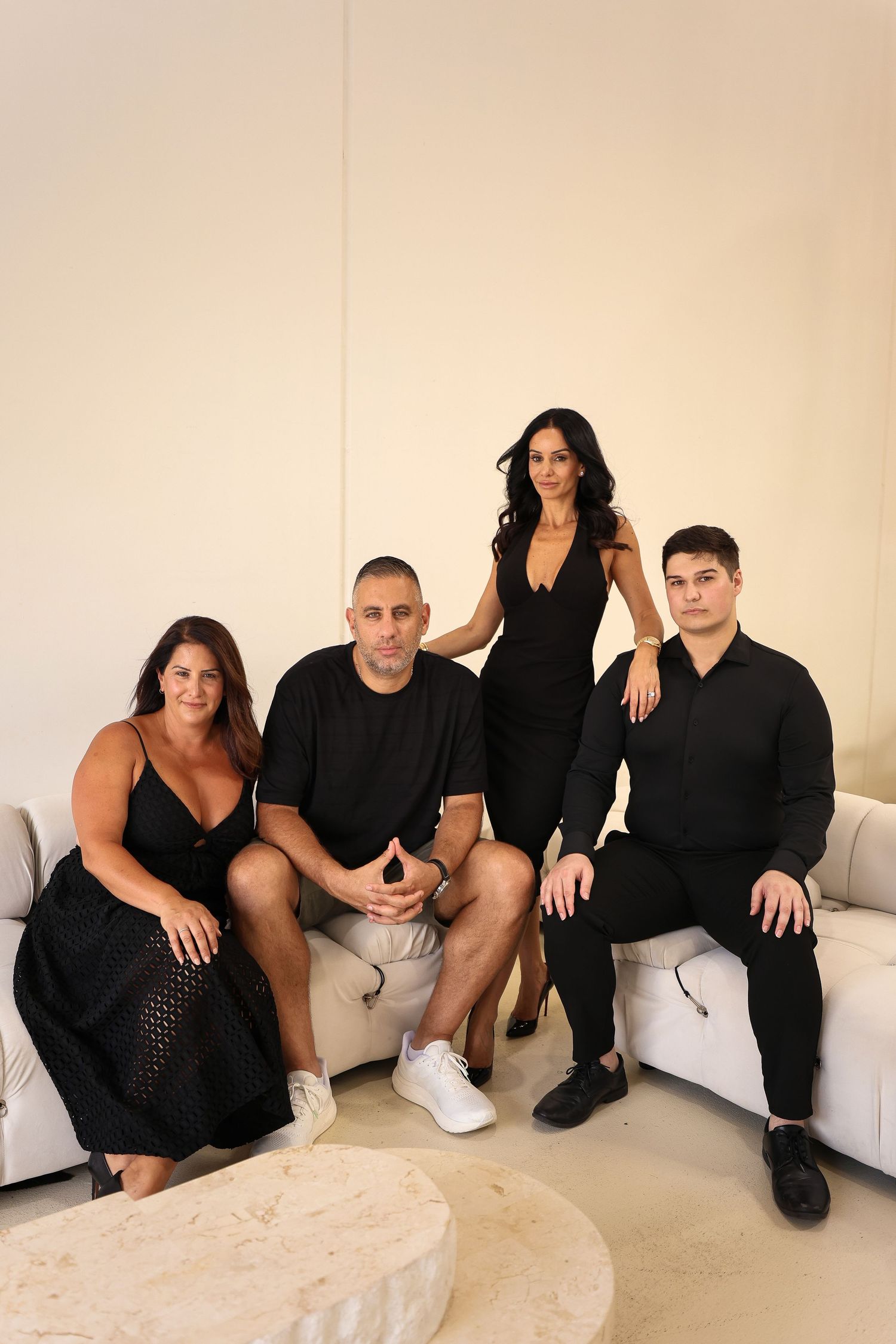 Group photo of four people dressed in black seated on white couch for business portrait.