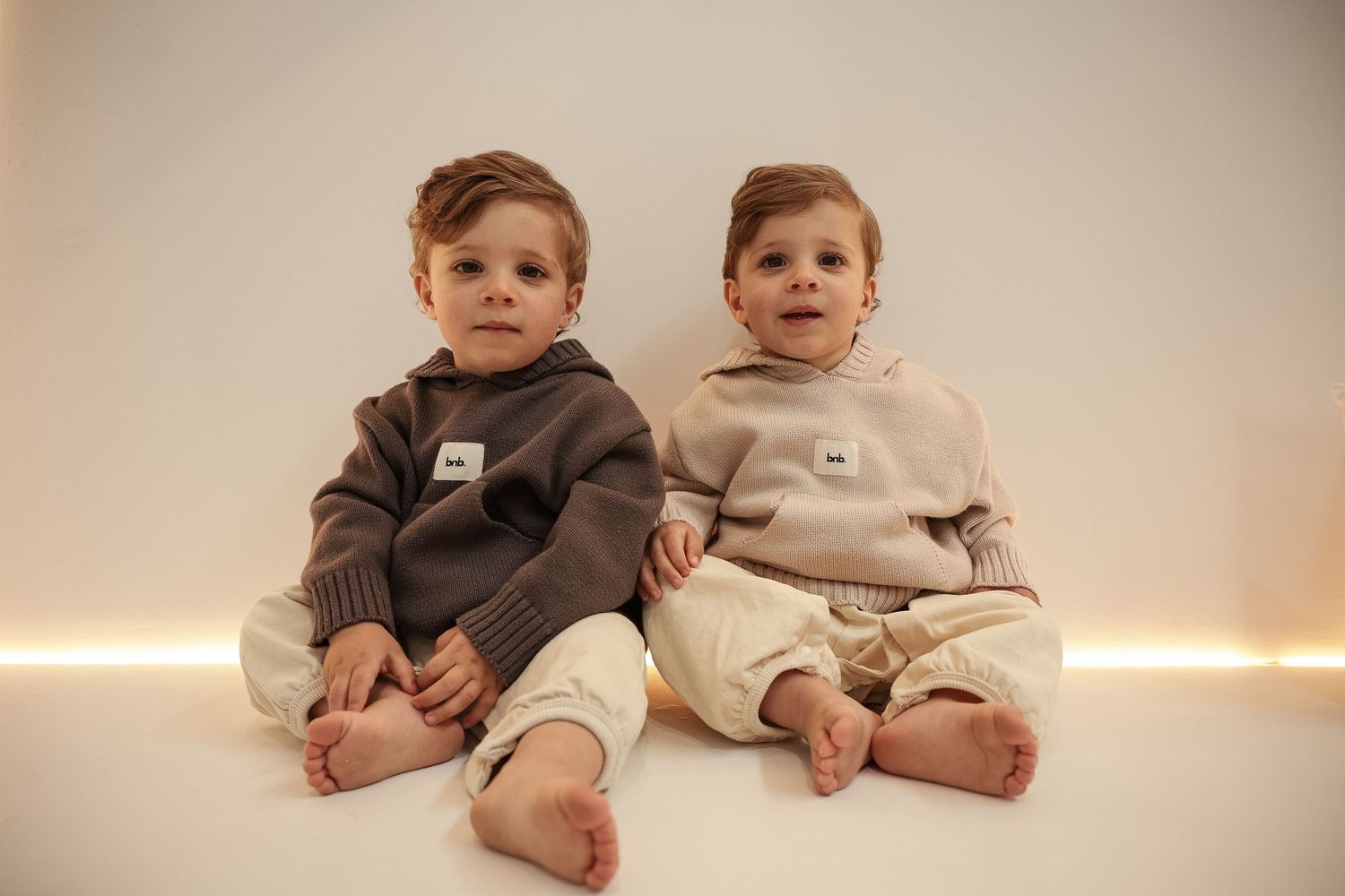 Two young children in matching beige and brown hooded sweatshirts sitting together.