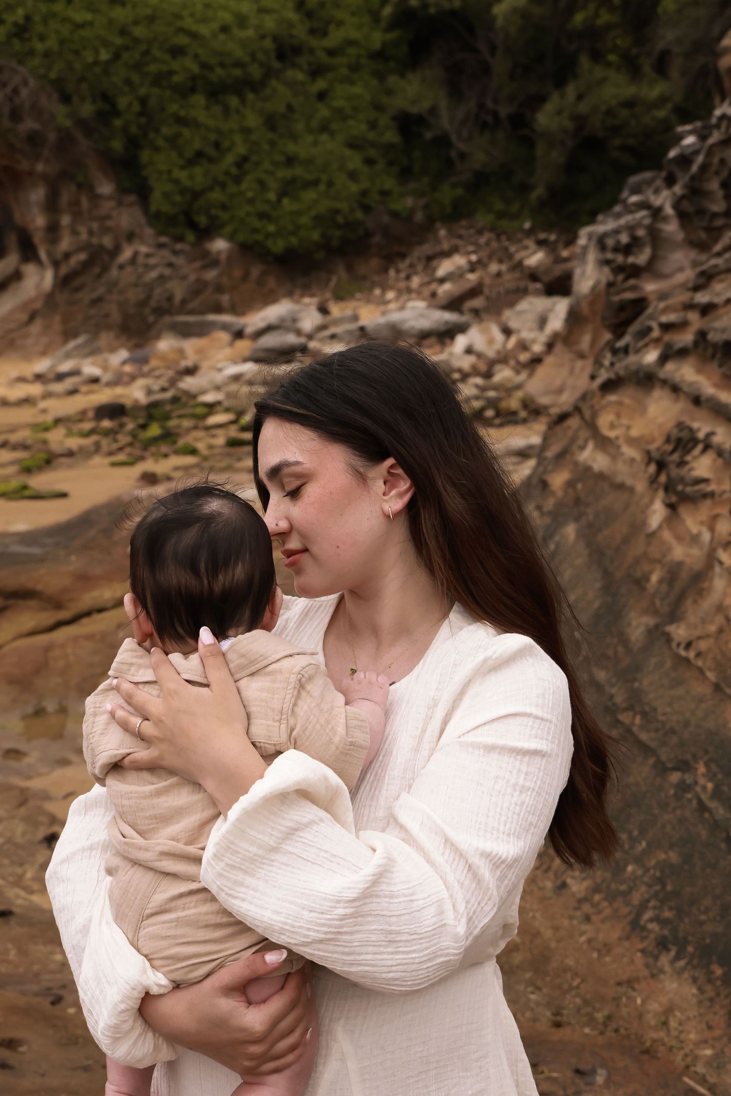 Mother and child in white outfits sharing an intimate moment against rocky cliffs.