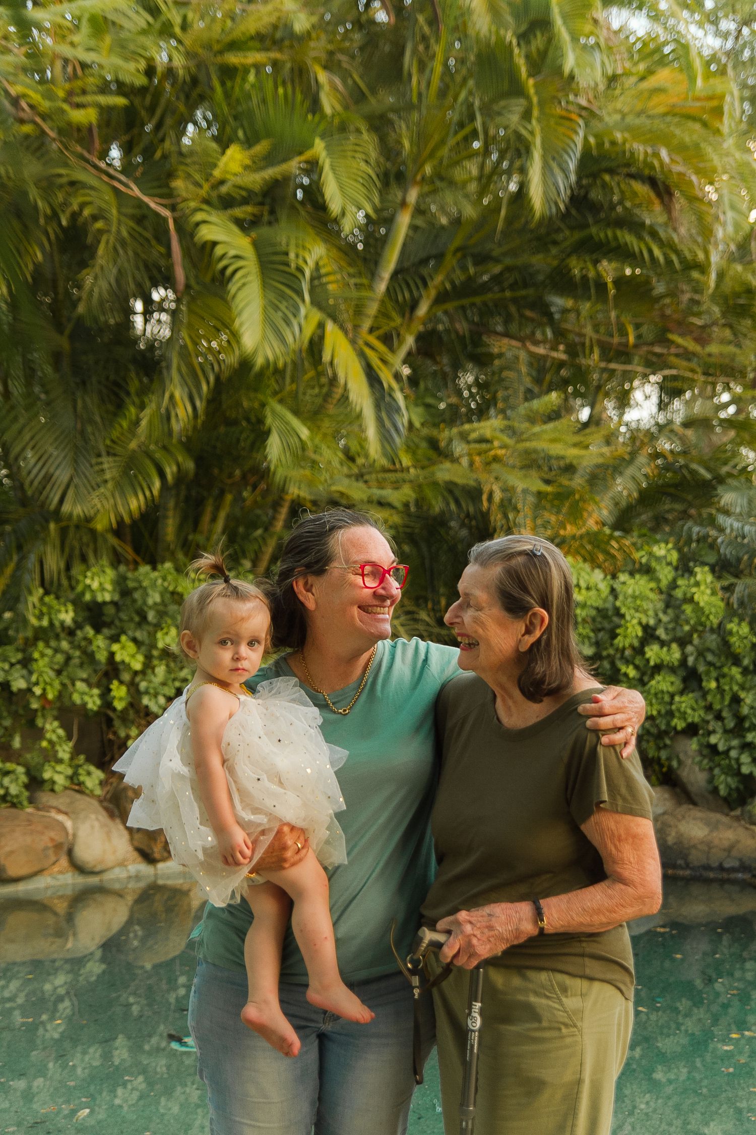 Three generations gather by tropical pool surrounded by palm trees.