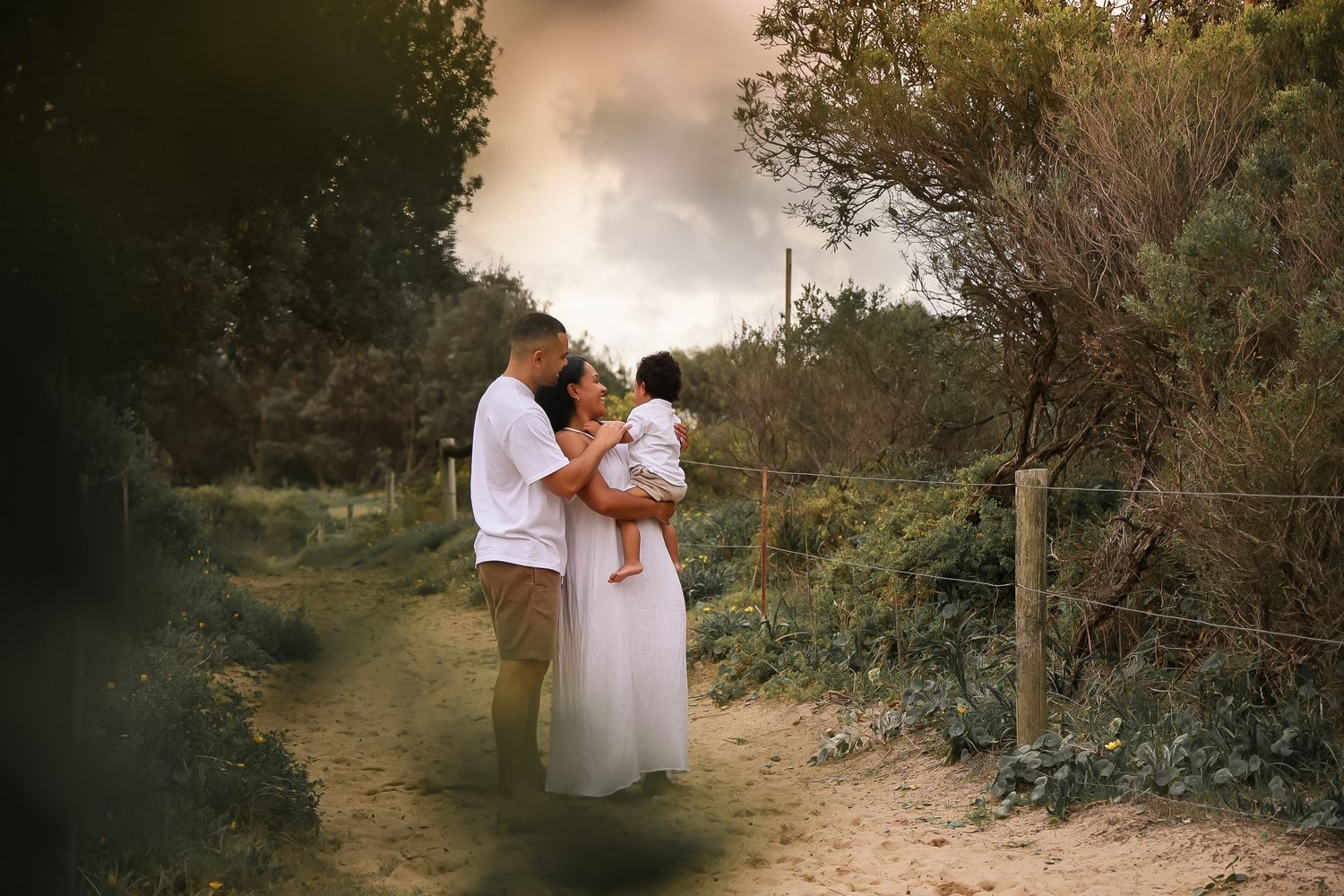 A couple embraces on a nature trail during golden hour surrounded by lush greenery.