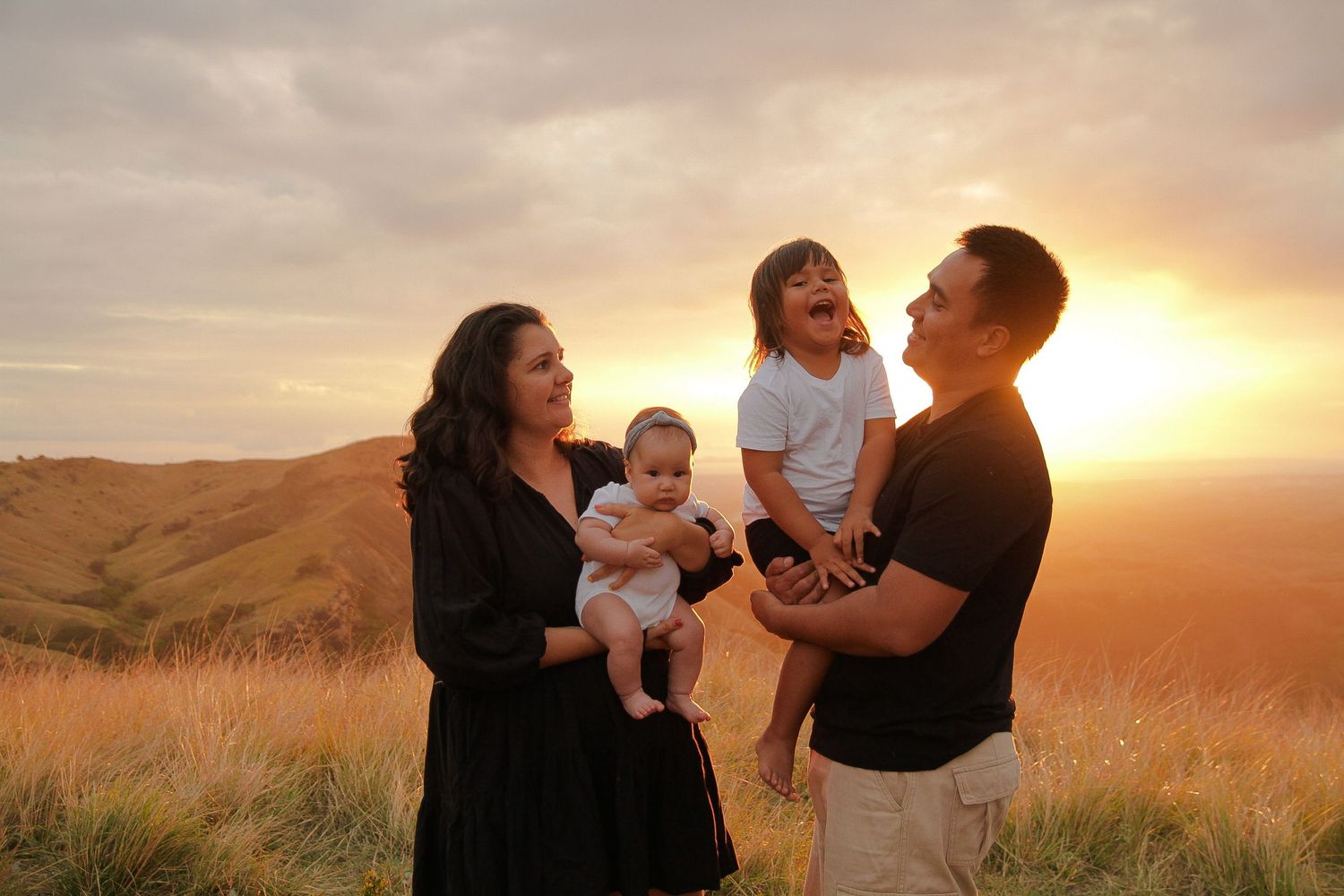 Family laughs together against golden sunset on rolling hills.