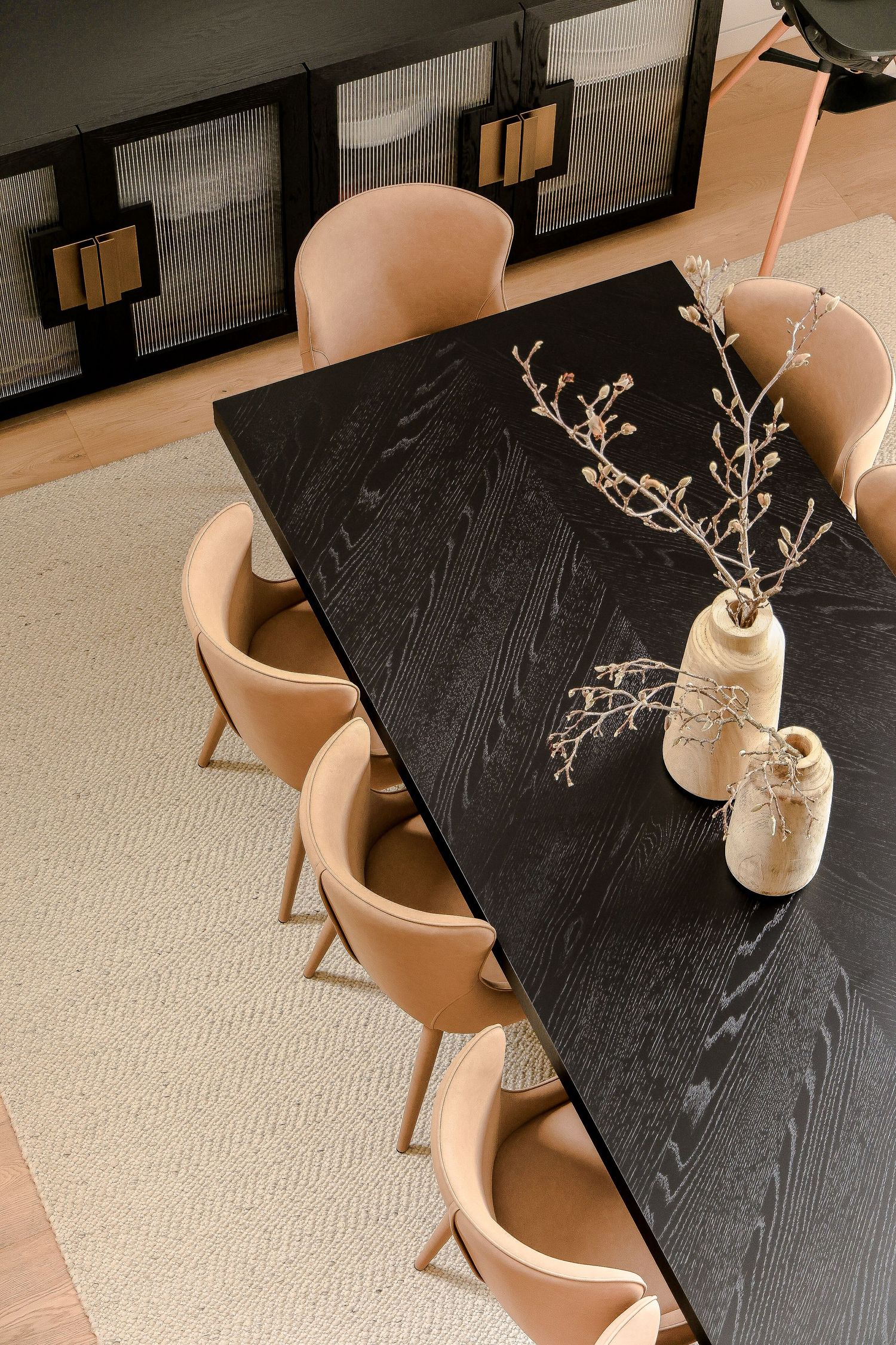 Black dining table with beige chairs and decorative vases containing dried branches.