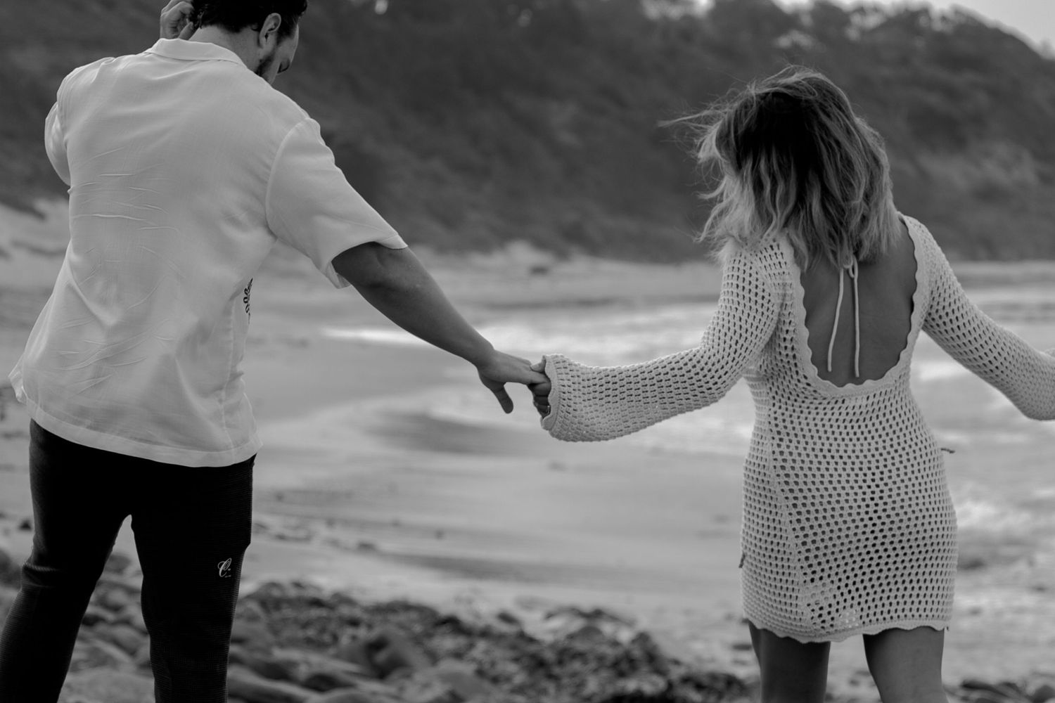 A couple holding hands walking along a scenic beach during sunset.