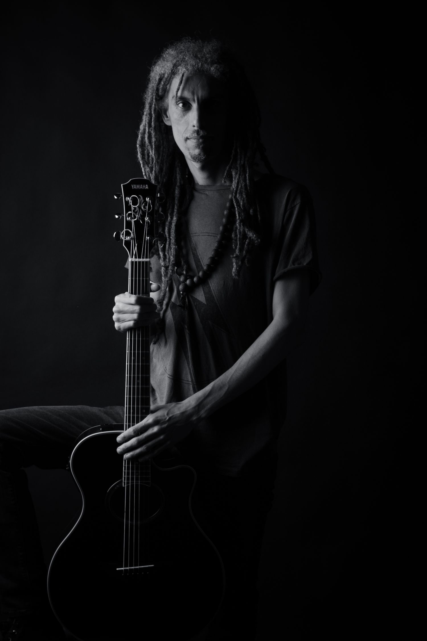 Moody black and white portrait of musician with dreadlocks holding acoustic guitar.
