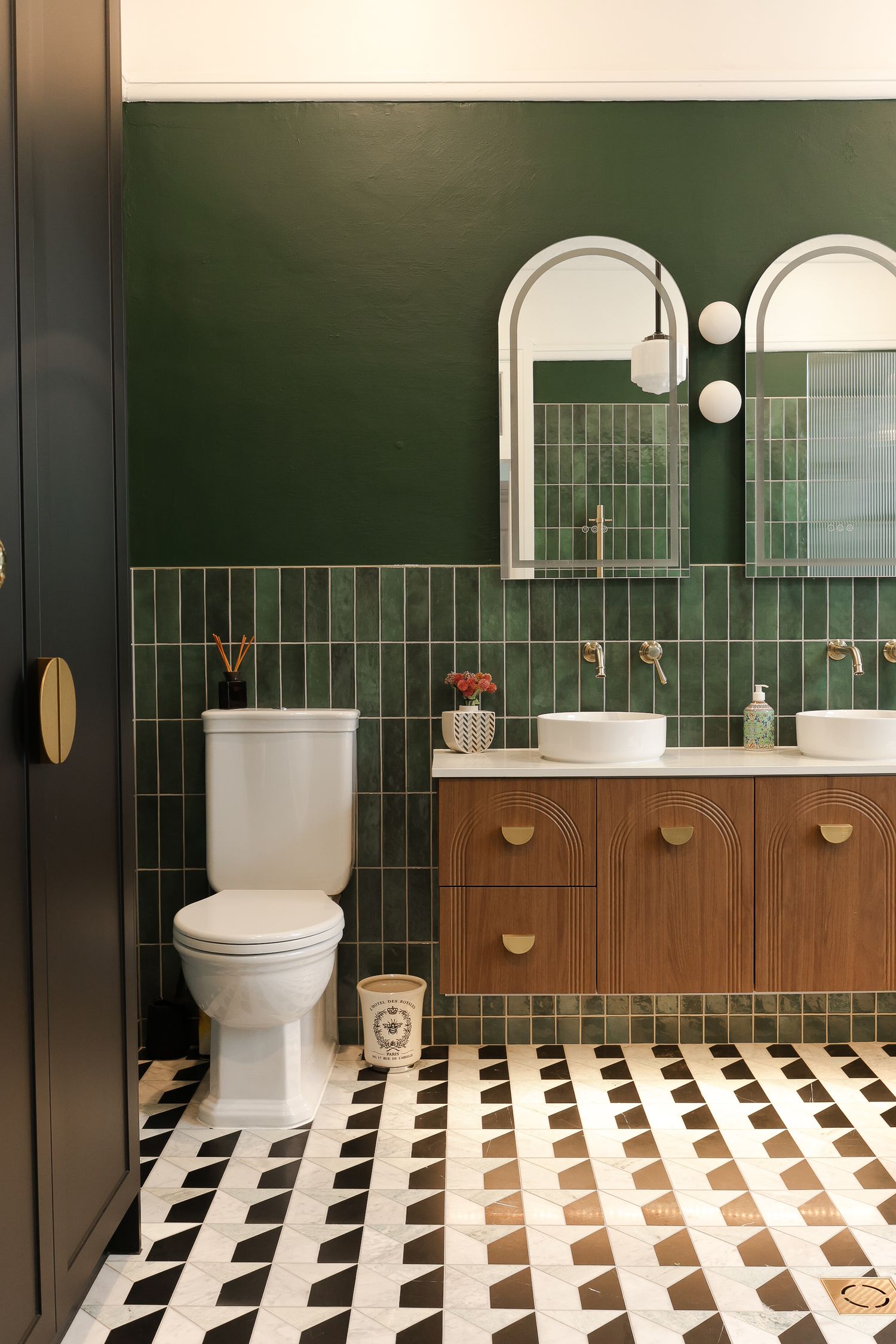 Luxurious bathroom featuring dark green tile walls, wooden vanity, and black and white patterned floor.