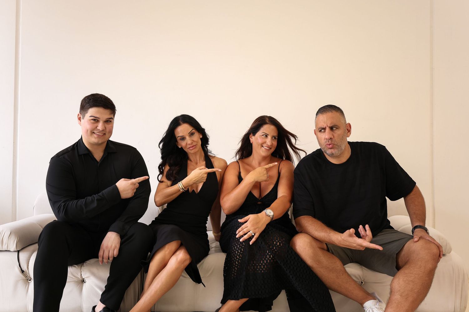 Four people sitting together on a white couch wearing coordinated black outfits.