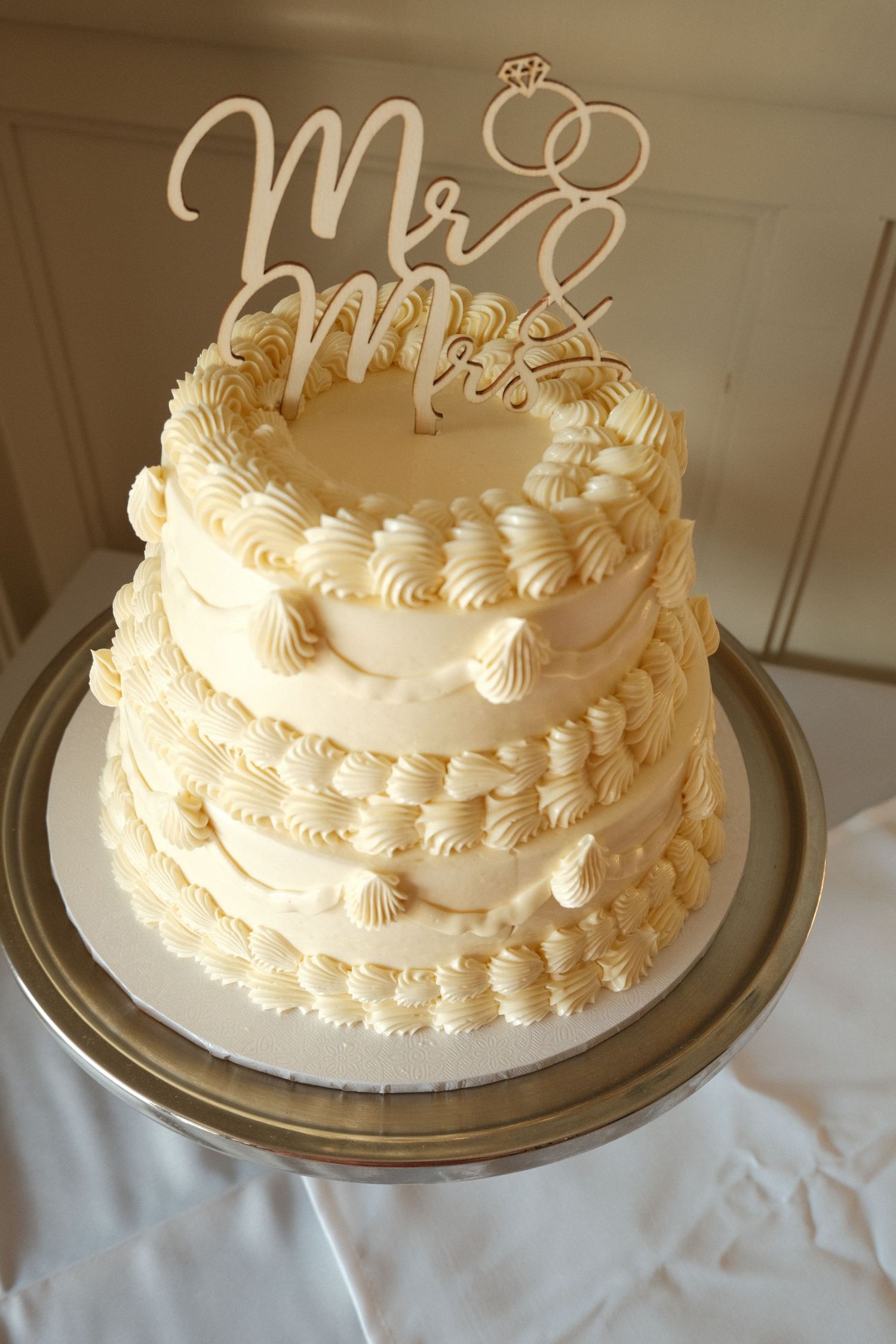 Elegant three-tier white wedding cake with piped frosting details and a Mr & Mrs topper.