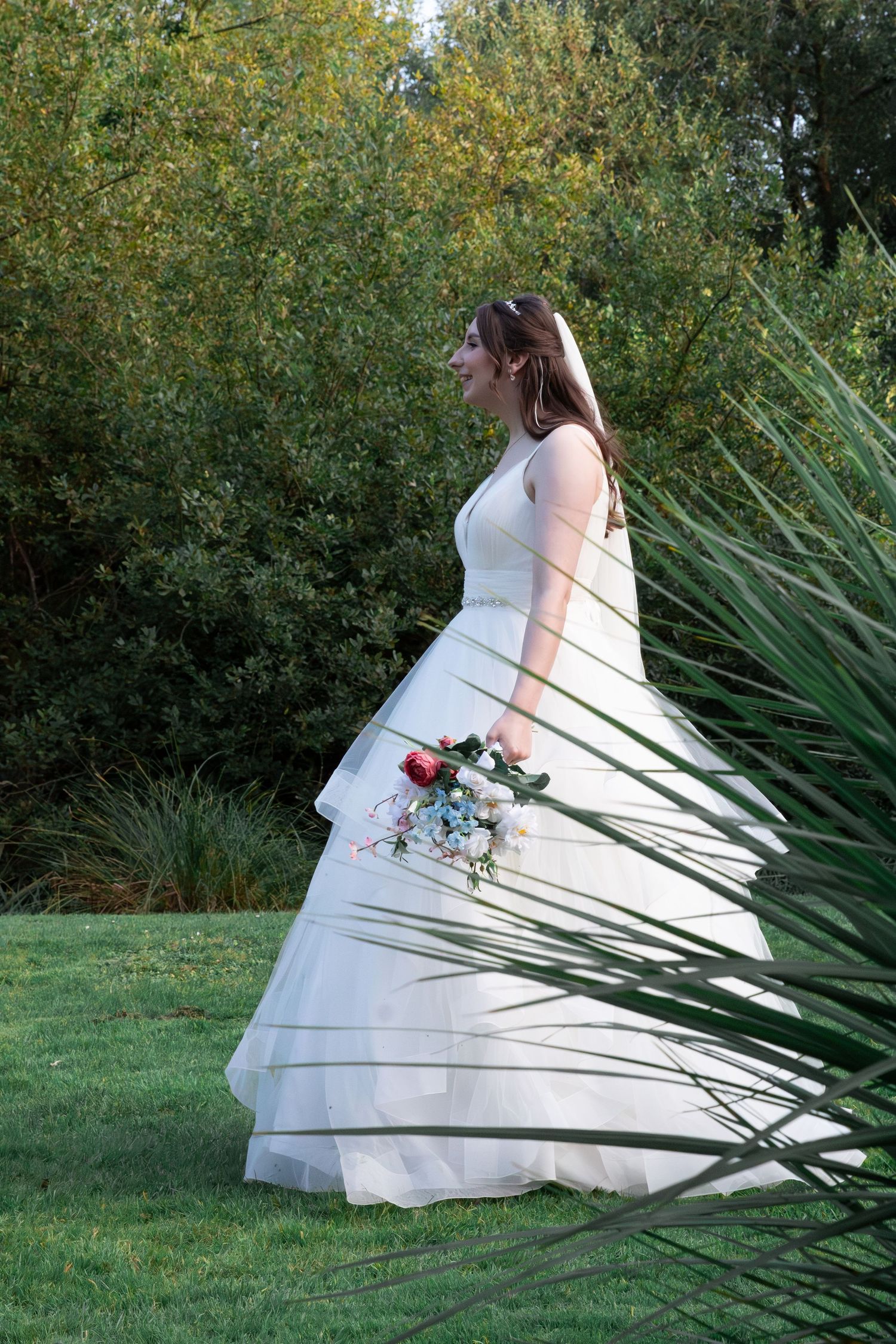 A bride in a white wedding gown poses near ornamental grasses holding a bouquet.