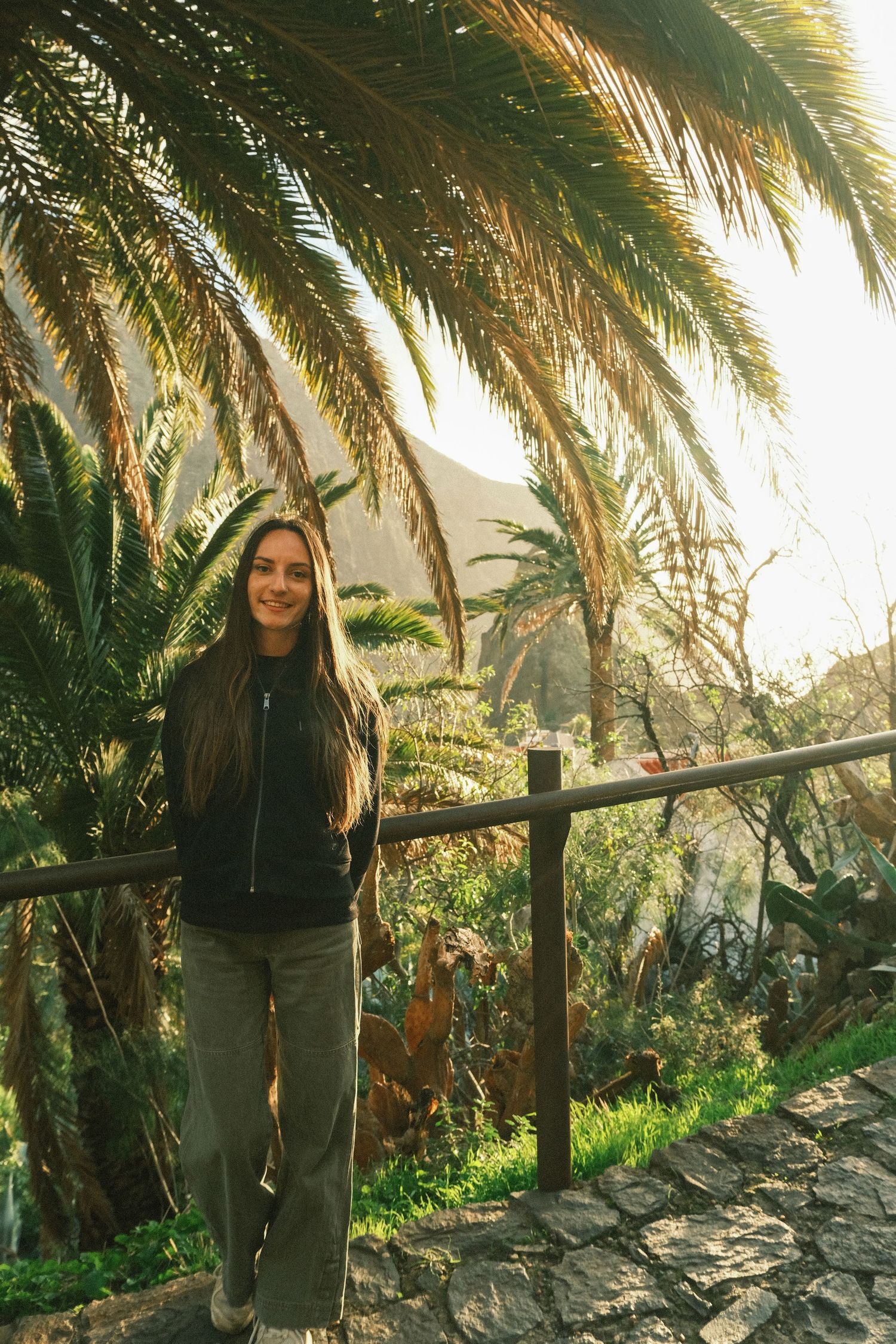 Mollie on a scenic overlook with palm trees and mountains in the background.