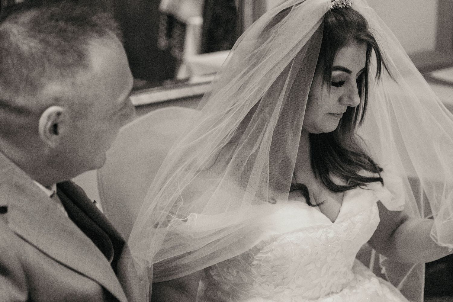 A tender black and white wedding moment with bride in lace veil.