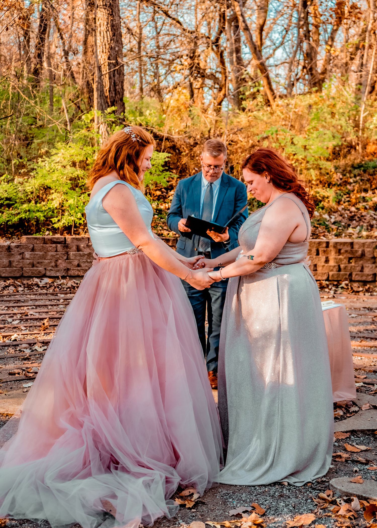 Two brides, hand-in-hand, being prayed over by the officiating pastor.