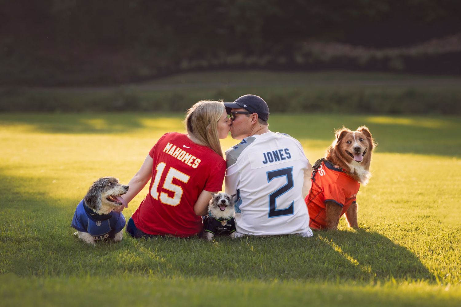 Couple kissing in Maryville, TN park with three dogs sitting happily, all wearing sport jerseys