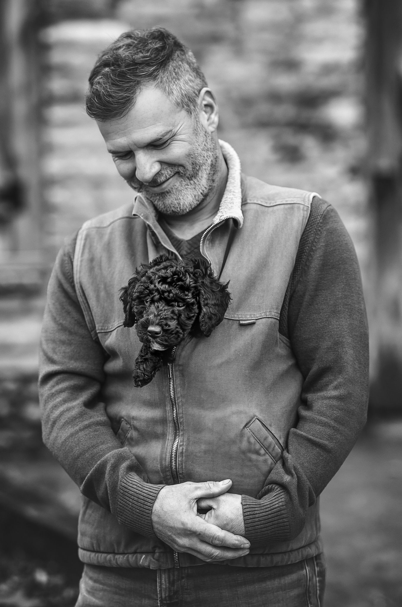 Black and white photo of man smiling, looking down at black puppy he has tucked into his vest during pet session at Norris Lake in Tennessee